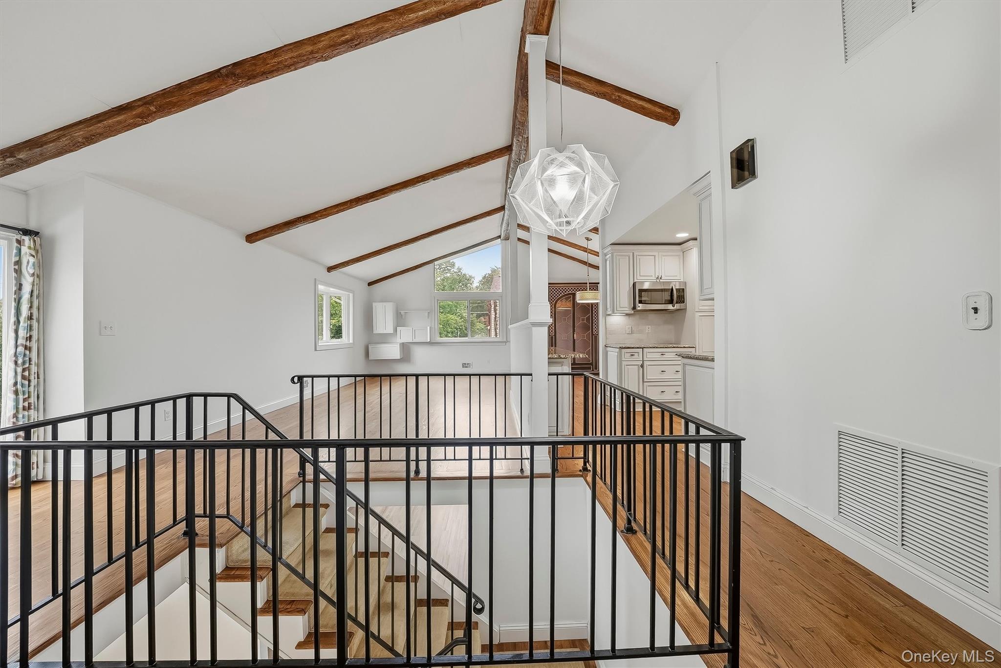 Open landing with exposed ceiling beams, hardwood floors, black railings, and a view into the kitchen.