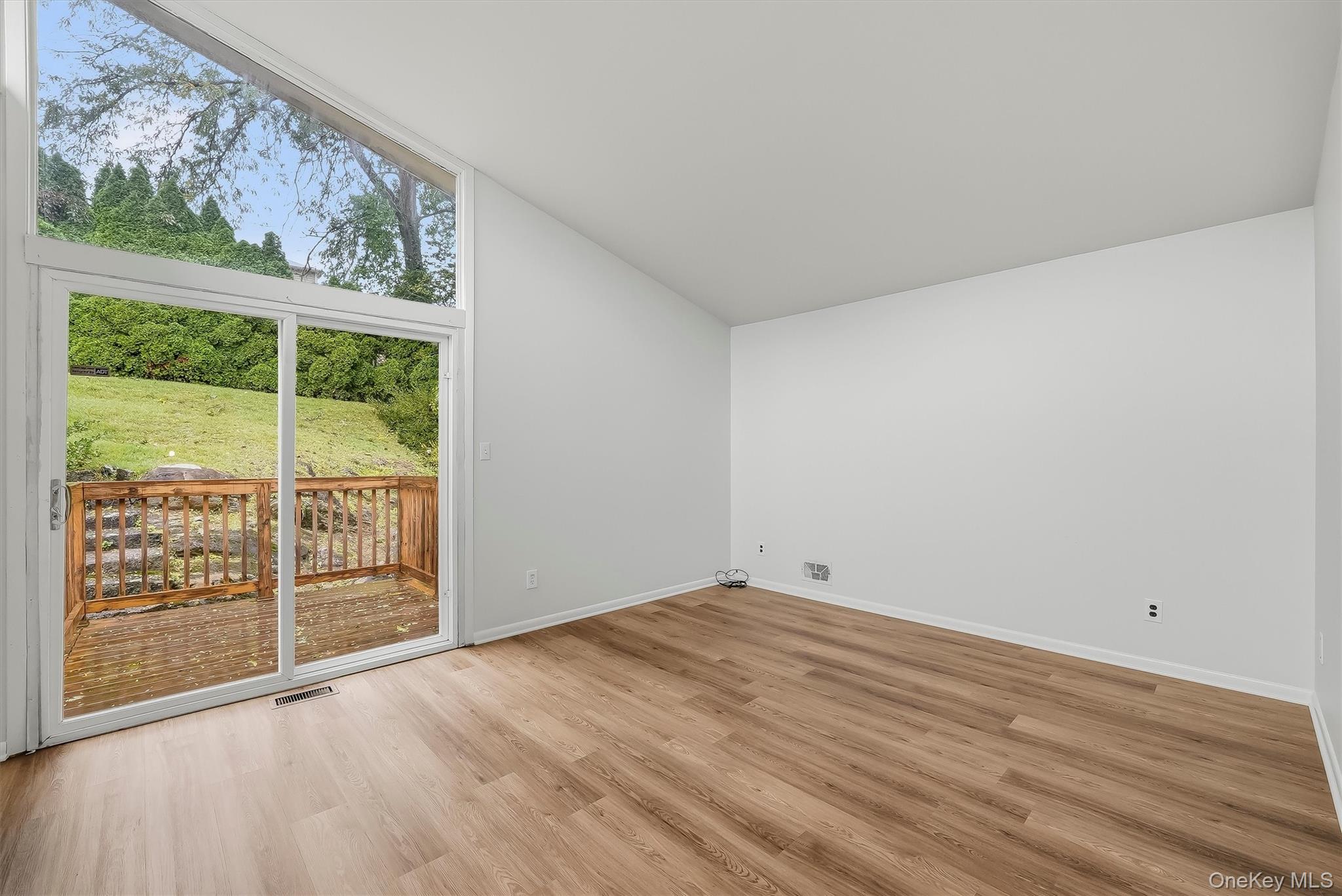 Vacant room with wood-look floors, a sloped ceiling, and sliding glass doors to a wooden deck.