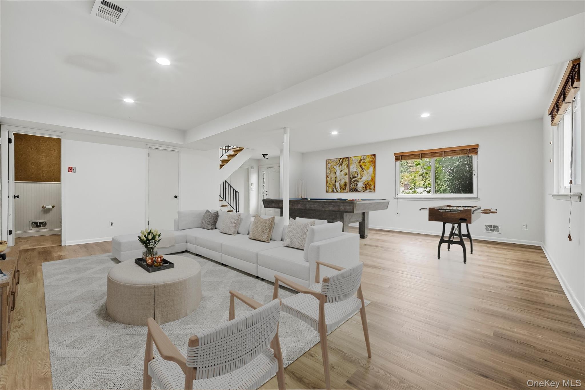 Open-plan living room with a white sectional, light wood floors, pool table, and foosball table.