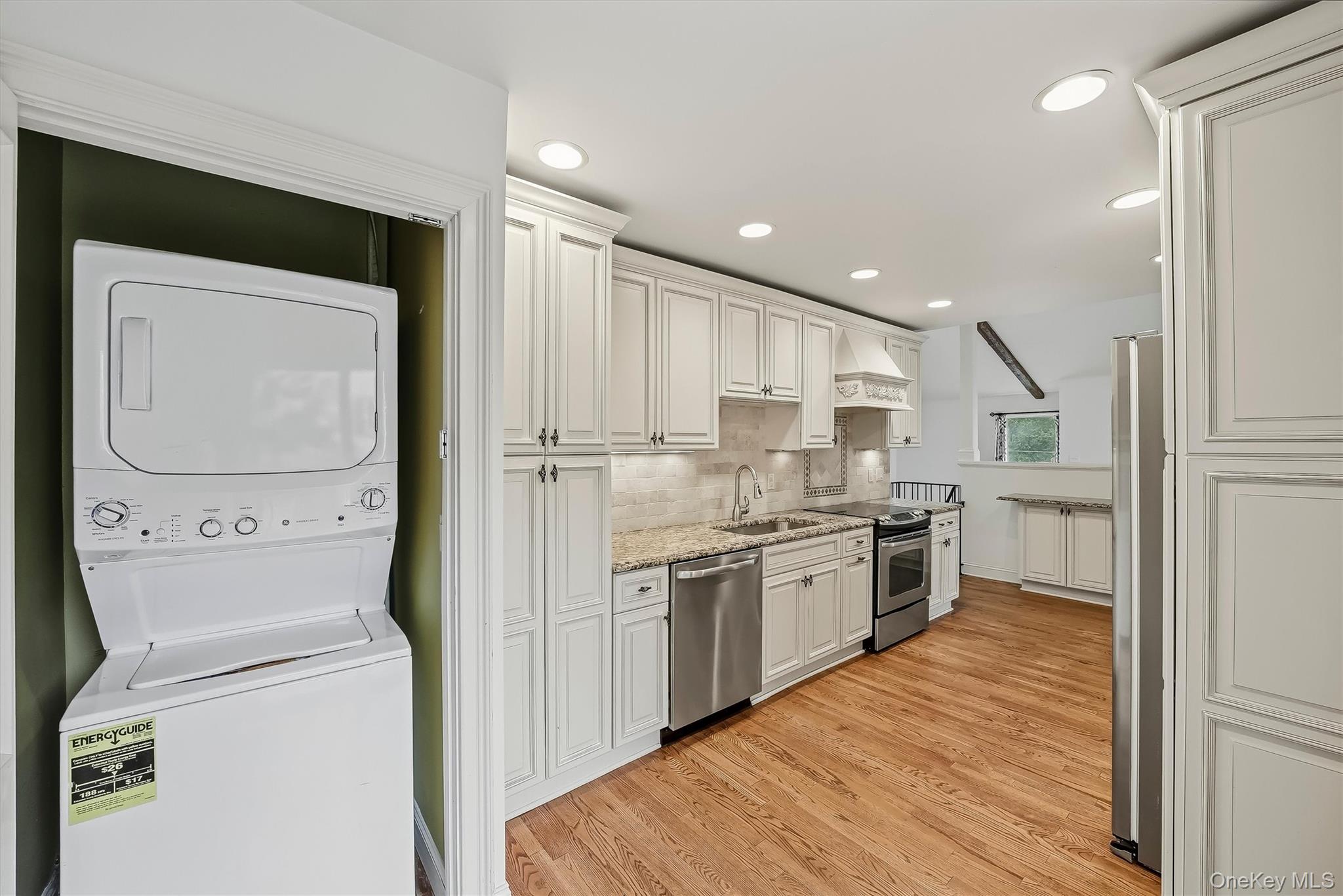 Kitchen with white paneled cabinets, granite counters, stainless appliances, and an adjacent washer-dryer closet.
