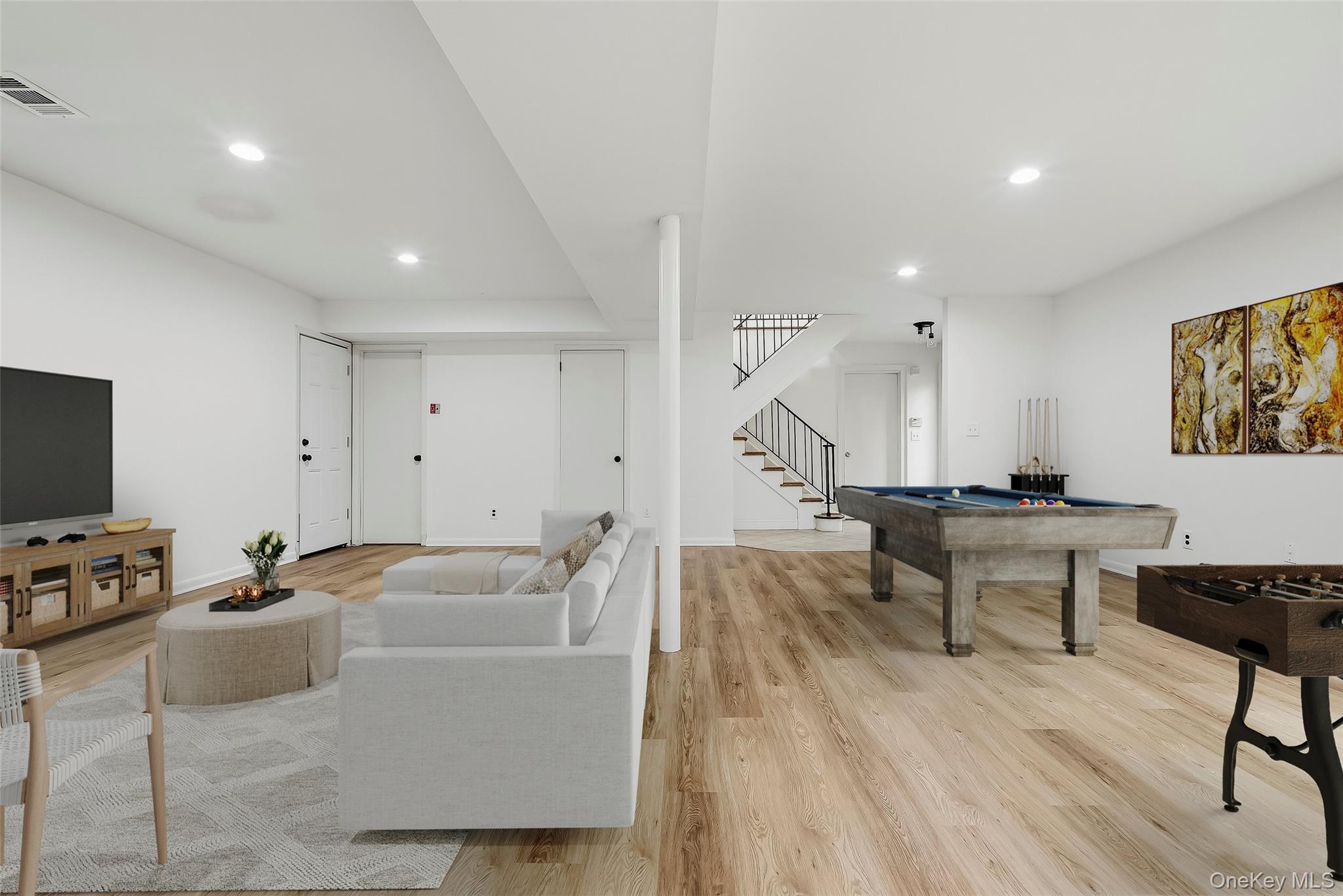 Recreation room with a white sofa, pool table, foosball table, and staircase.