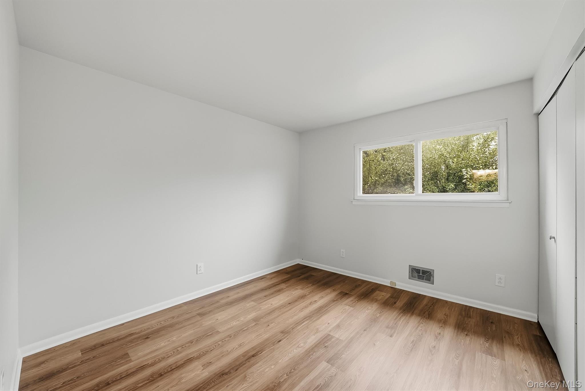 Empty room with warm wood floors, a wide window, and a built-in closet.