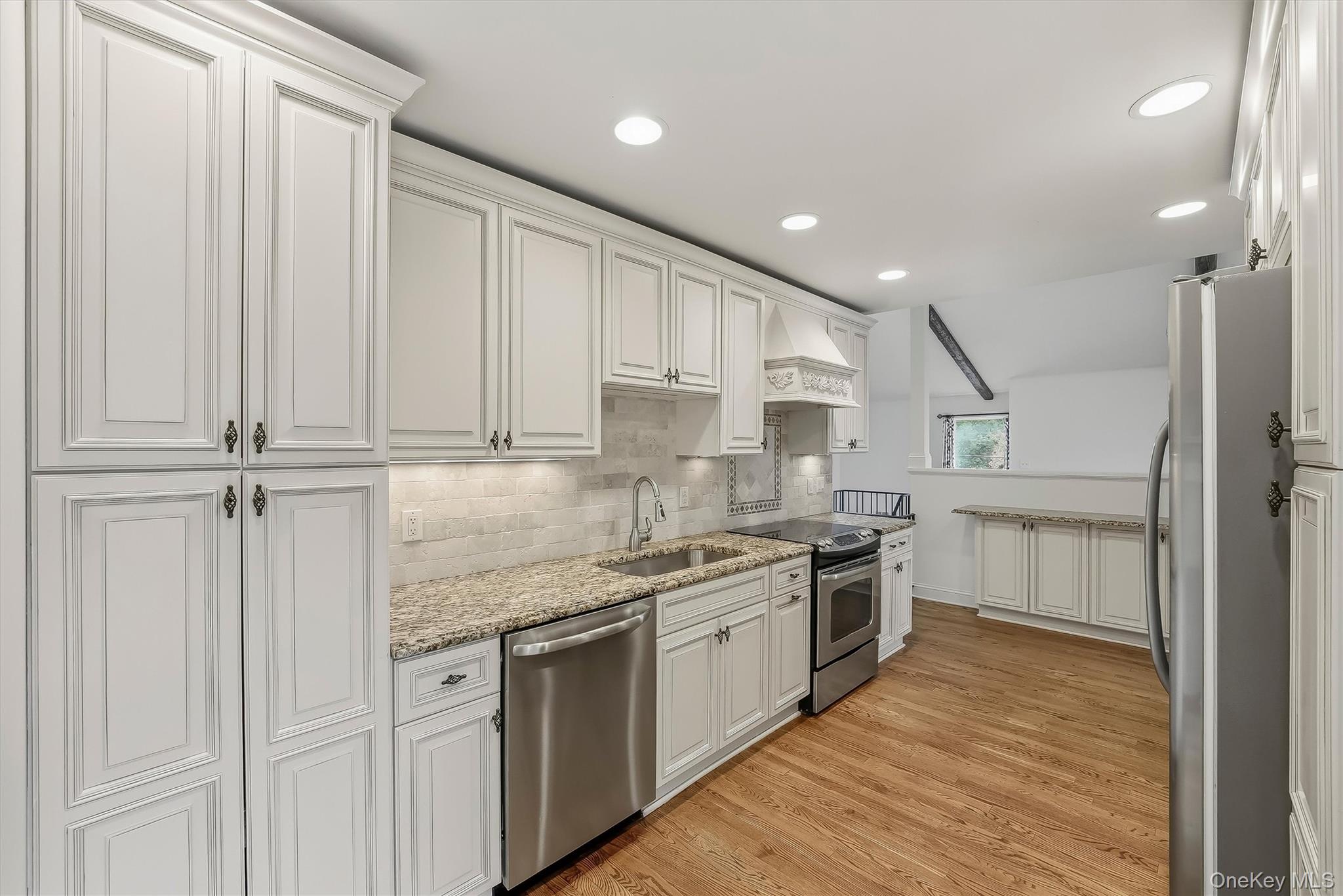 Kitchen with white paneled cabinets, granite counters, stainless steel appliances, and hardwood floors.