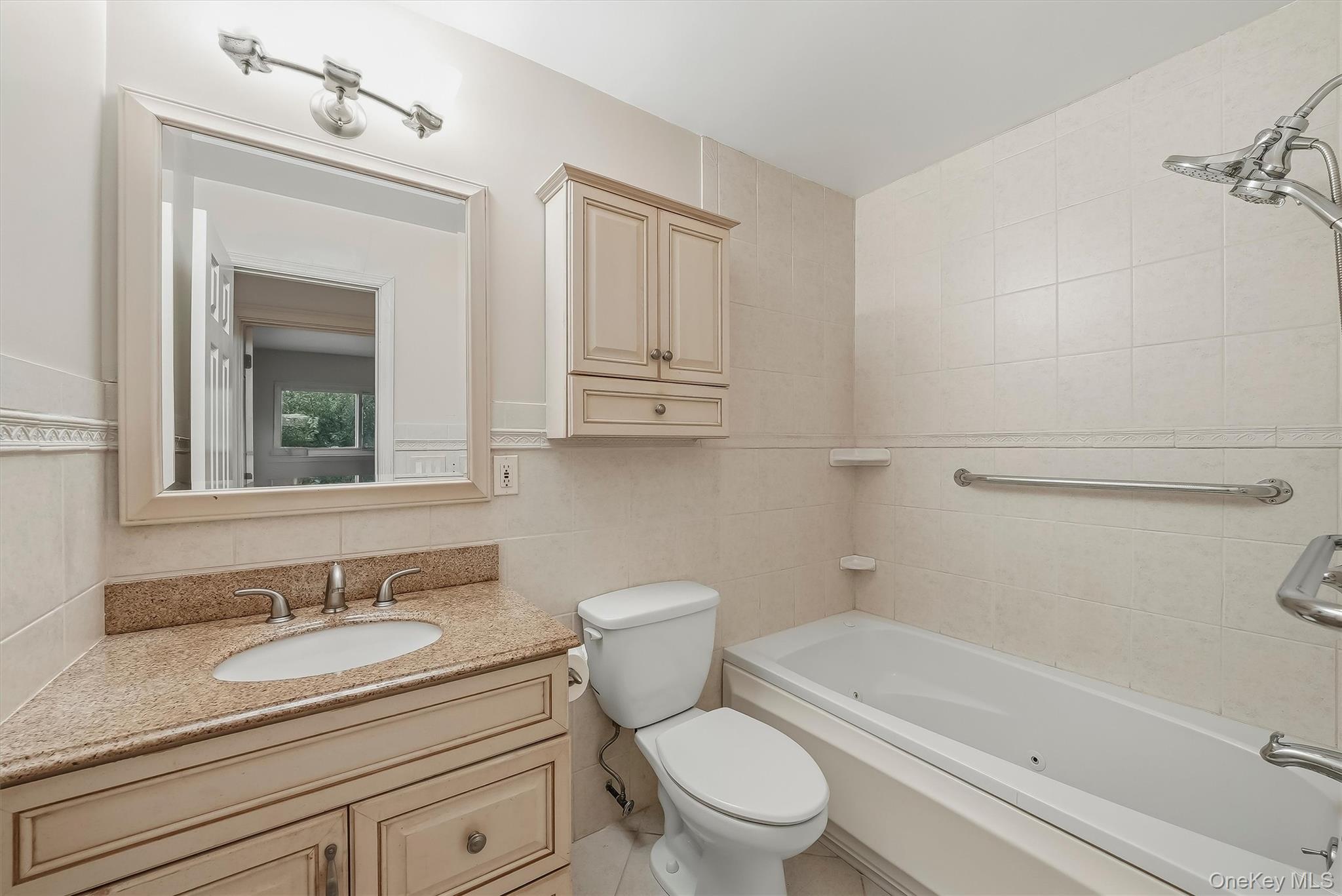 Bathroom with tiled tub and shower, grab bars, and a granite-topped vanity.