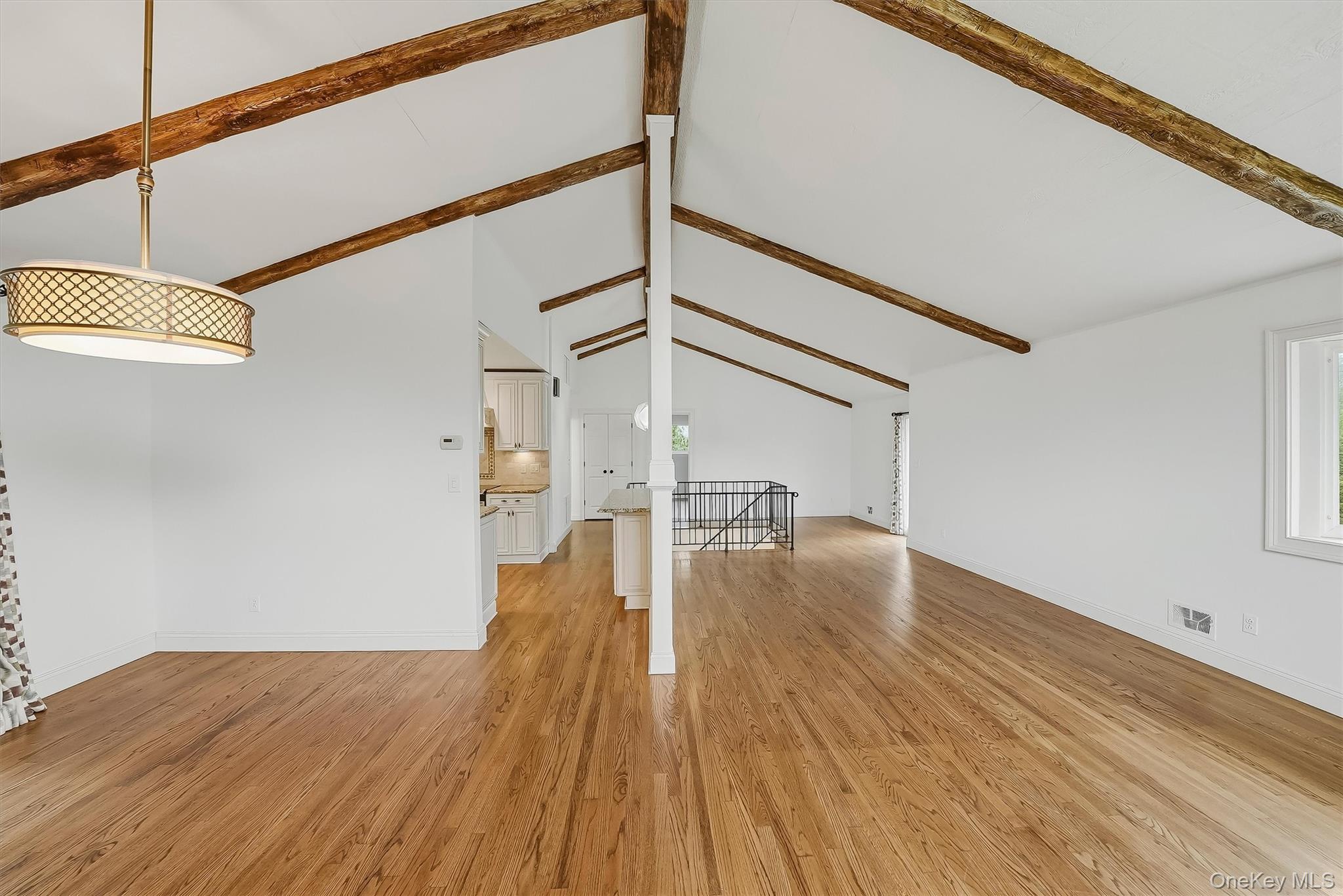 Vacant open living area with vaulted ceilings, exposed wood beams, and hardwood floors.