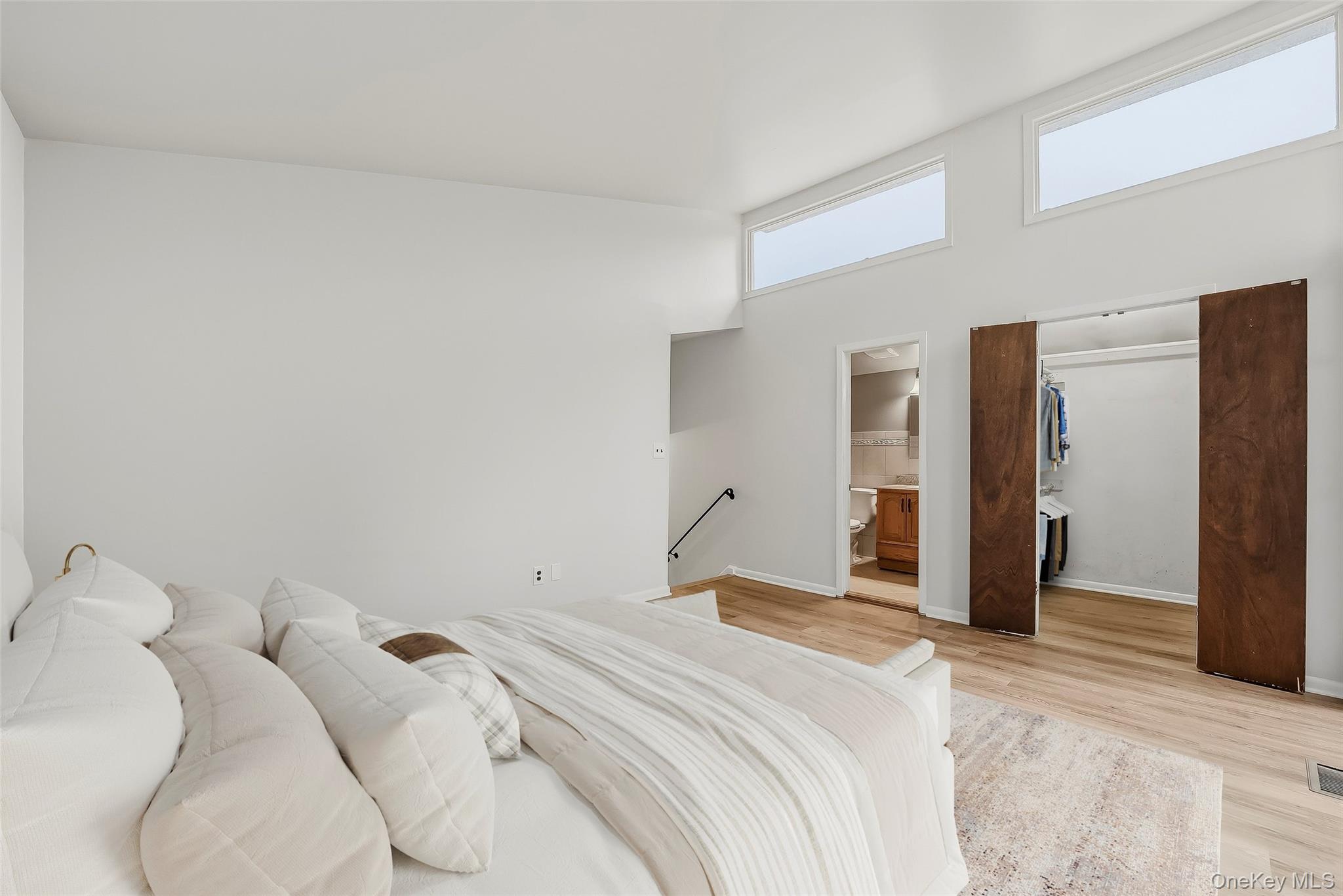 Bedroom with a white bed, high clerestory windows, open closet, and adjoining bathroom doorway.