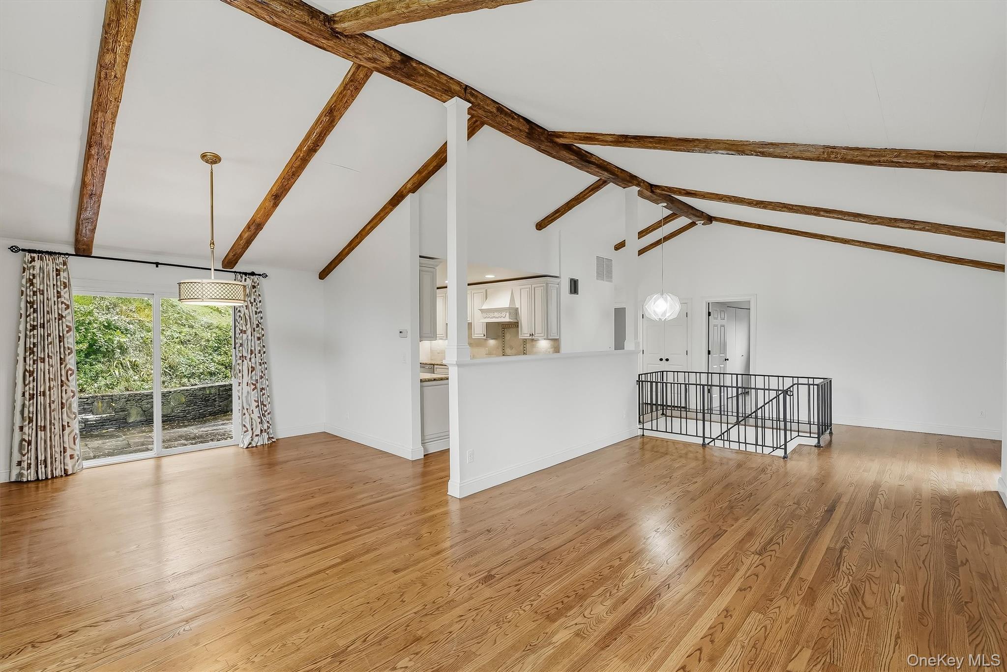 Open living area with vaulted exposed-beam ceiling, hardwood floors, and sliding glass doors to a patio.