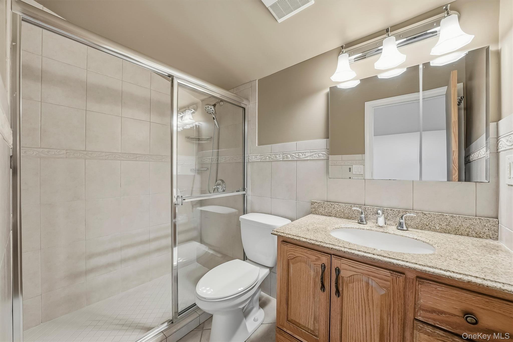 Bathroom with a glass shower, tiled walls, and a wood vanity with granite countertop.