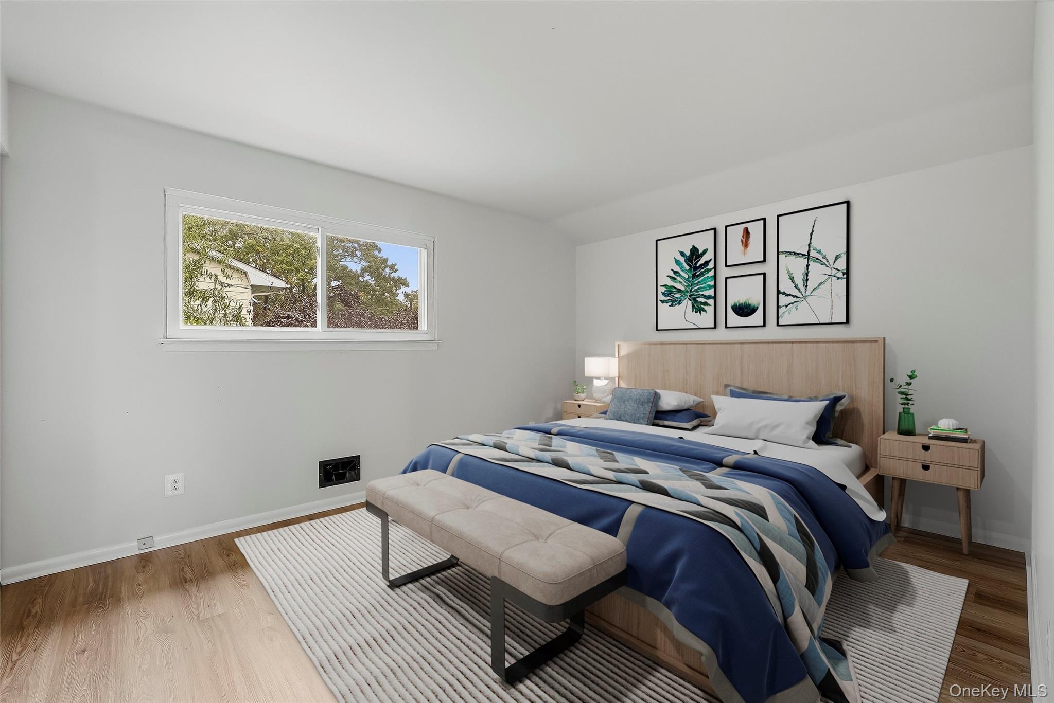 Staged bedroom with blue-and-gray bedding, botanical wall art, and a light wood headboard.