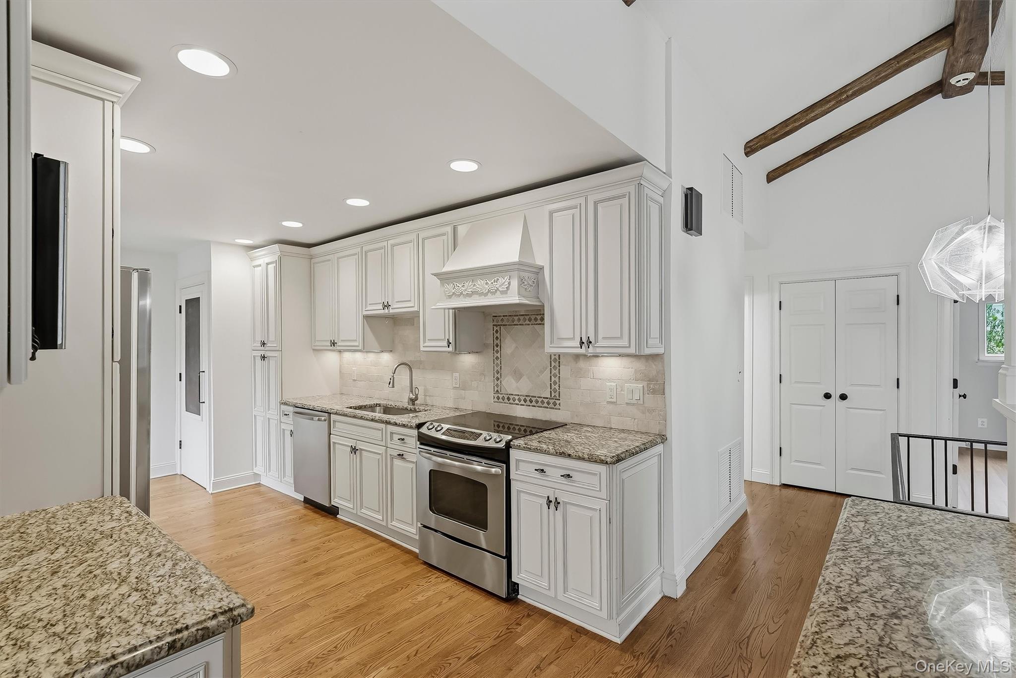 Kitchen with white cabinetry, granite counters, stainless appliances, and exposed ceiling beams.