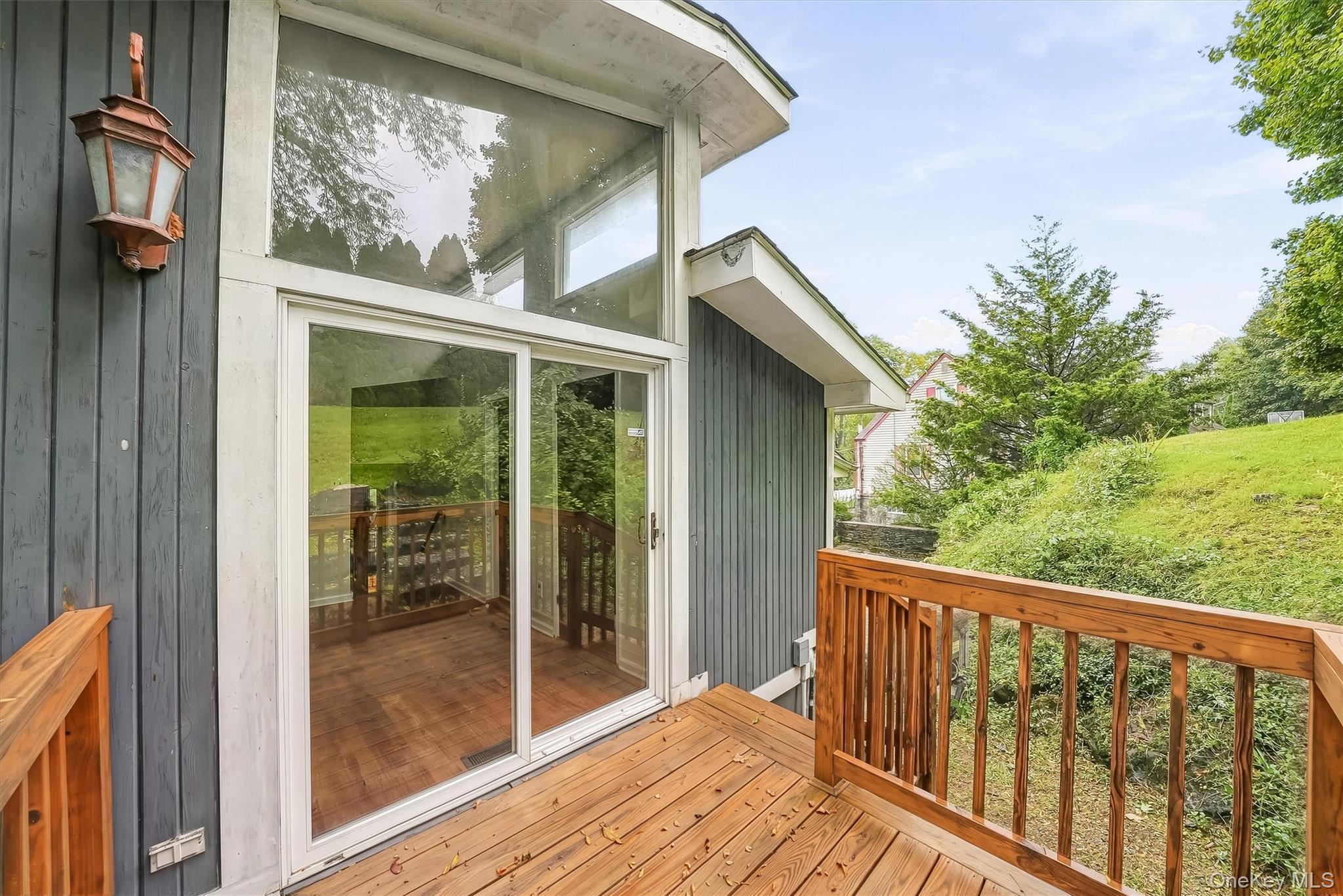 Wooden deck beside a large sliding glass door, with a leafy yard beyond the railing.