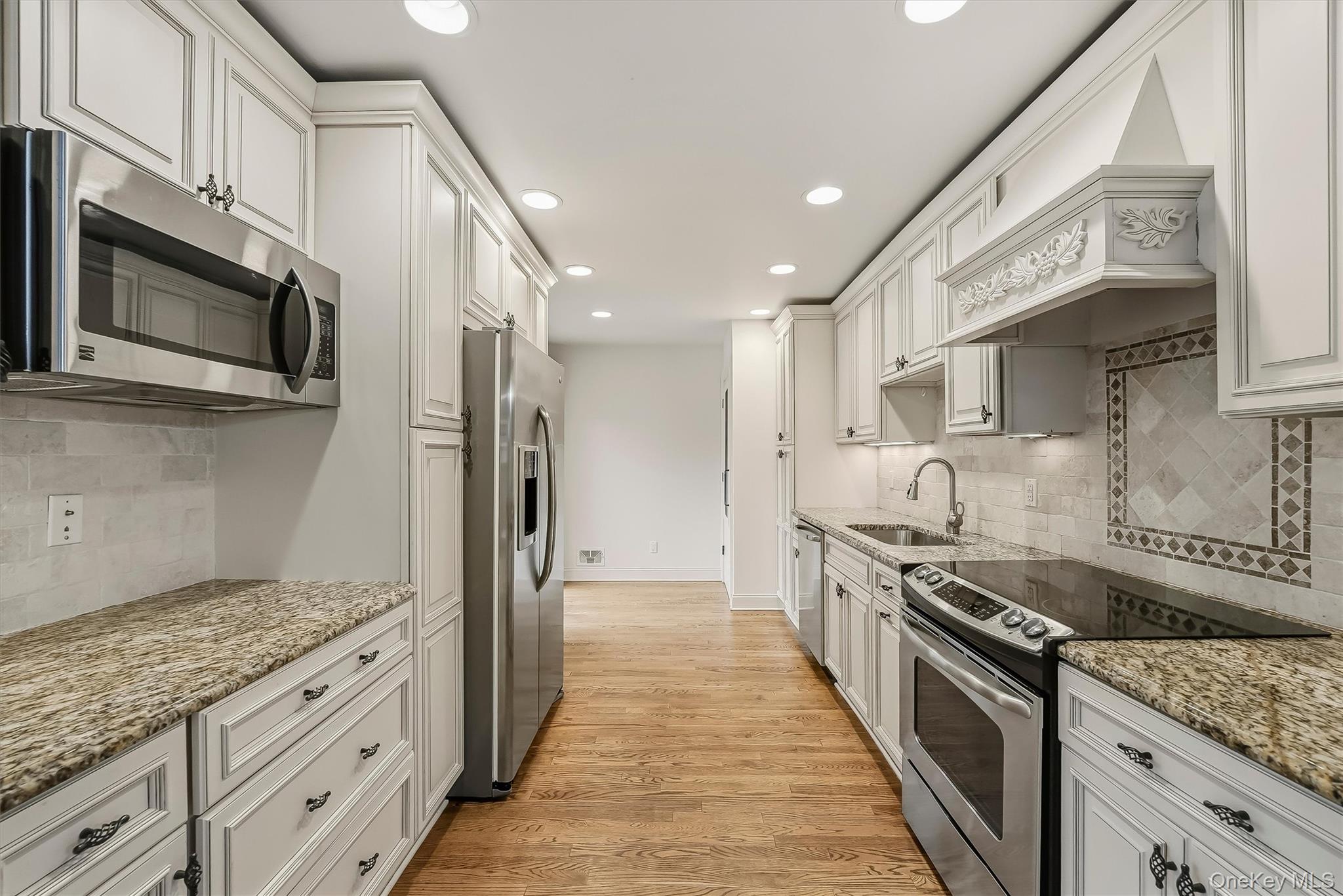 Kitchen with white cabinetry, granite counters, stainless steel appliances, and hardwood floors.