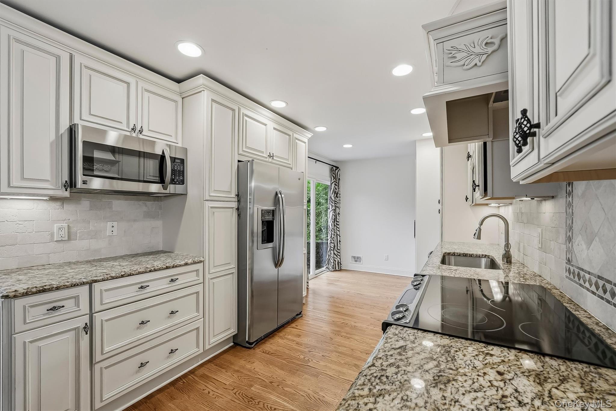 Kitchen with white cabinetry, granite counters, stainless steel appliances, and hardwood floors.