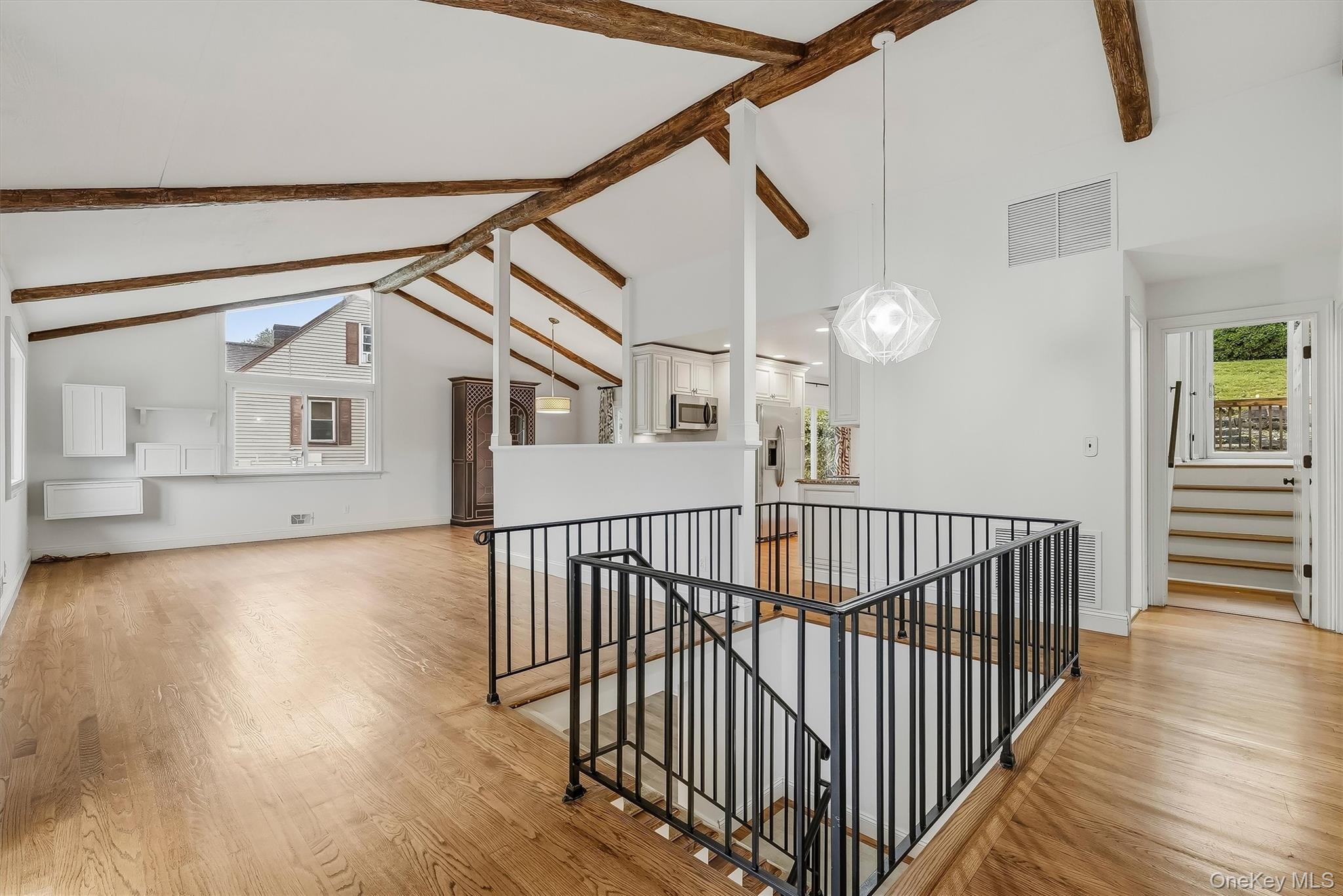 Open living area with vaulted wood-beam ceiling, hardwood floors, and black metal stair railing.