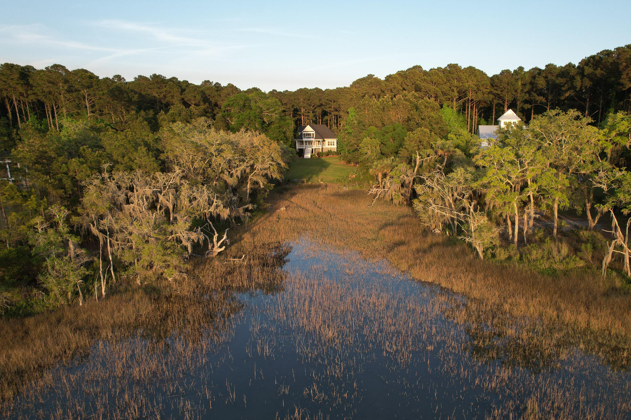 Aerial view of a tree-surrounded house beside a marsh creek.
