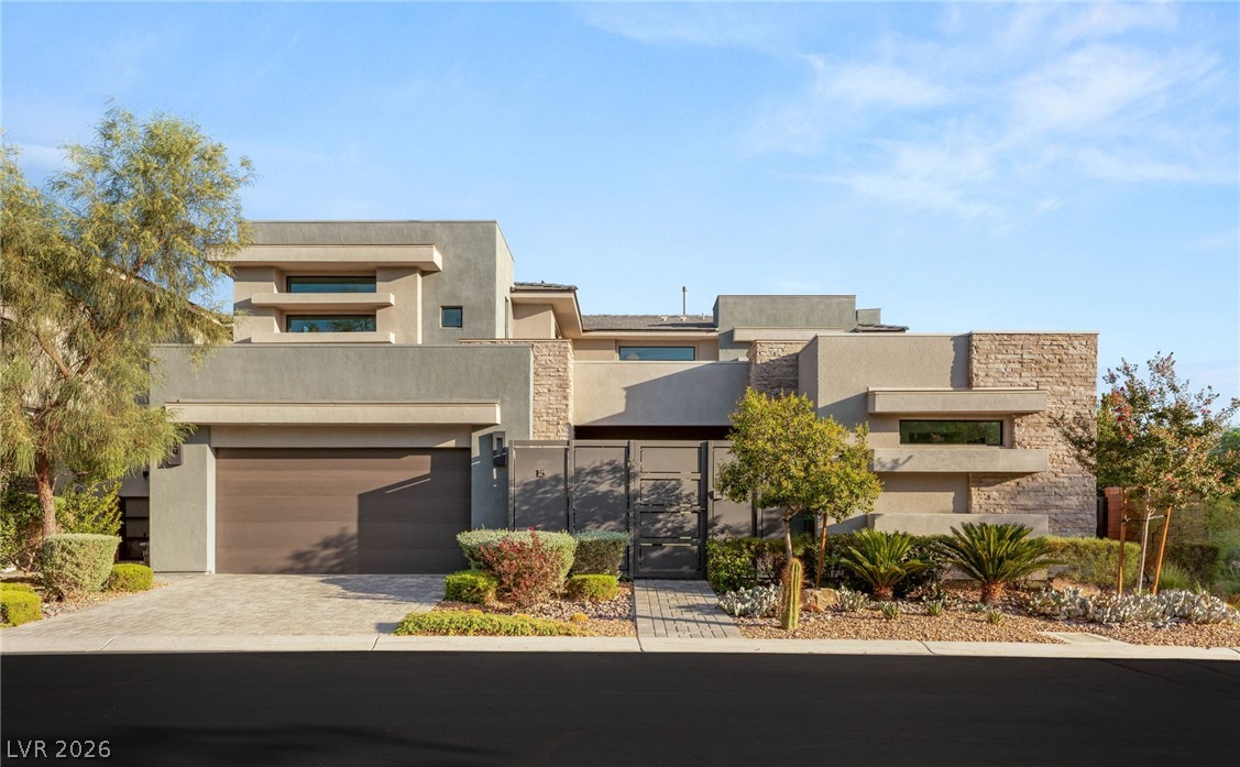 Modern home with a stone-accented facade, gated entry, and desert landscaping.