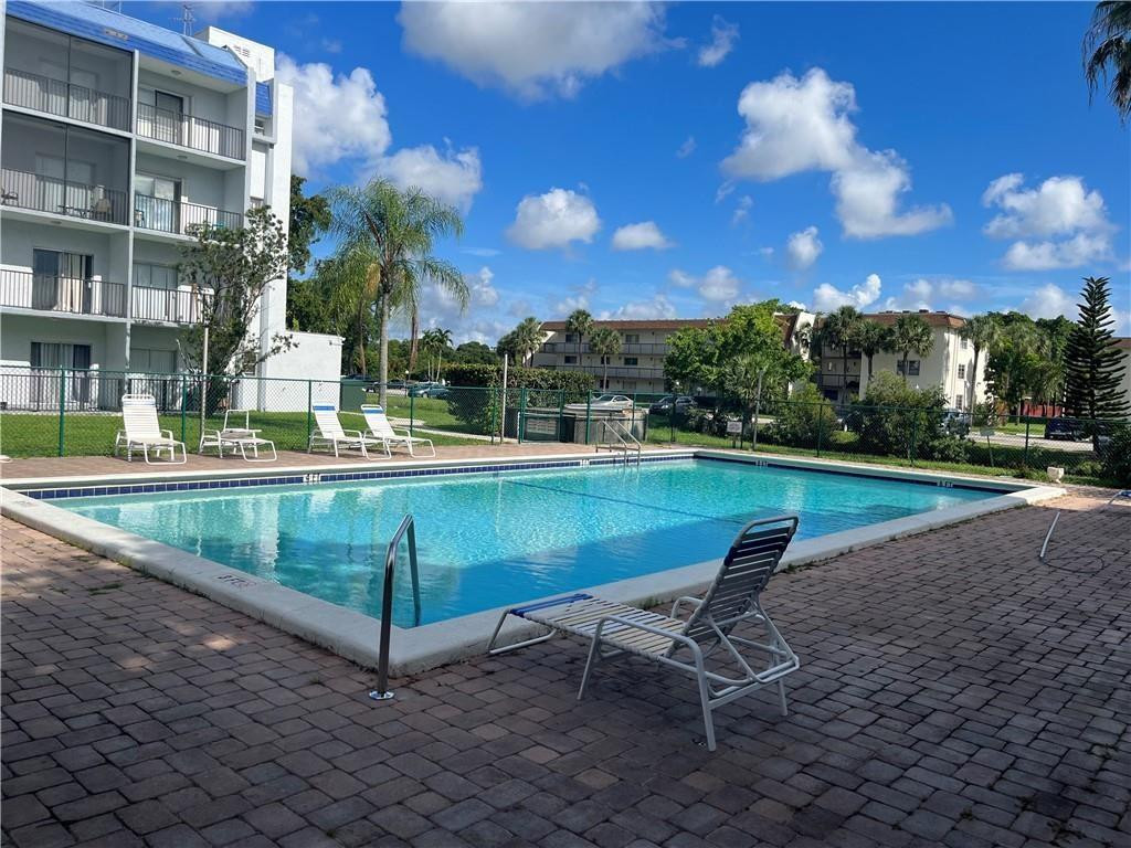 Condominium pool with lounge chairs on a brick-paved deck and apartment buildings beyond.