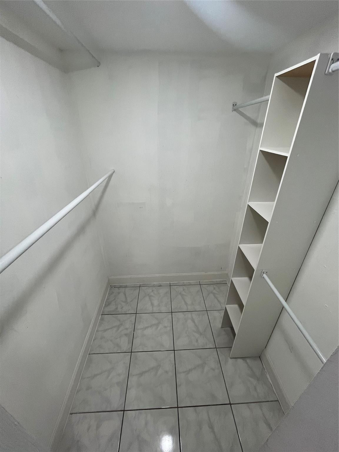 Empty walk-in closet with hanging rods, narrow shelving, and gray tile flooring.