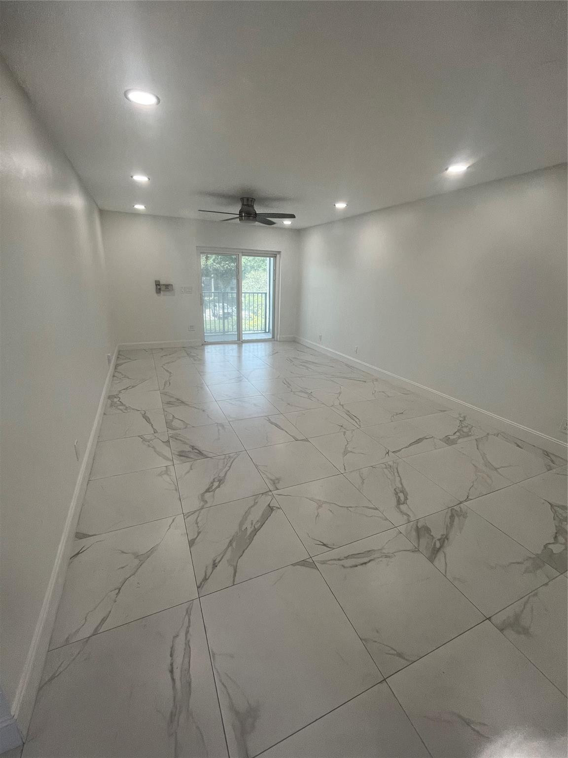 Vacant living room with marble-look tile floors, ceiling fan, and sliding glass doors to a balcony.