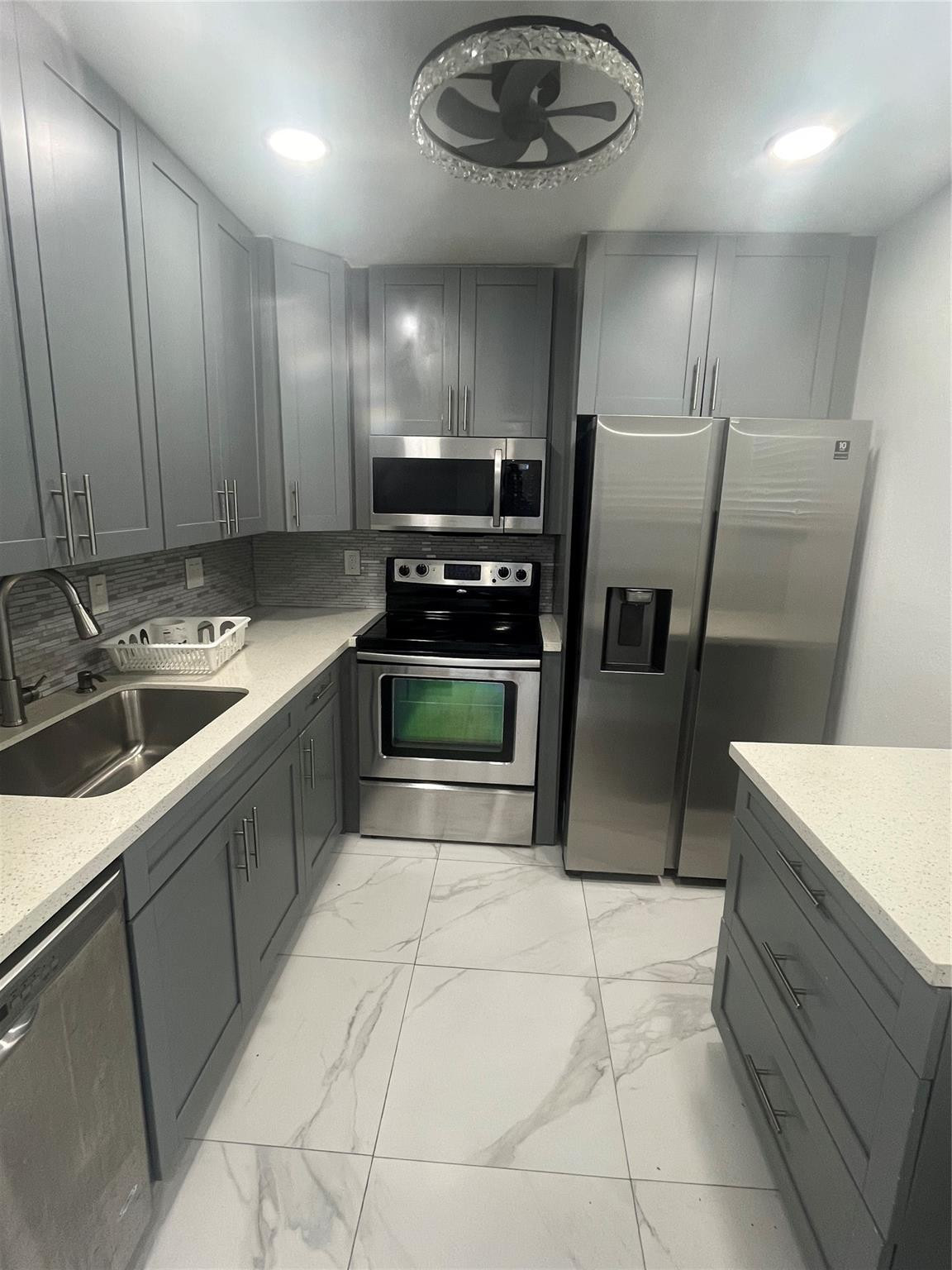 Galley kitchen with gray cabinets, stainless steel appliances, and marble-look tile flooring.