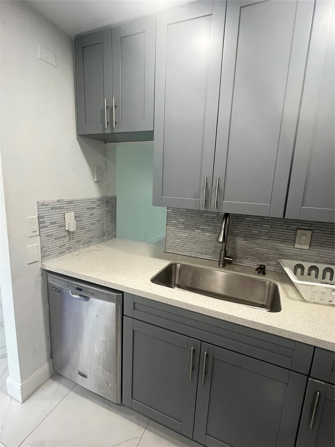 Kitchen with gray cabinets, a stainless-steel sink, and a narrow tile backsplash.