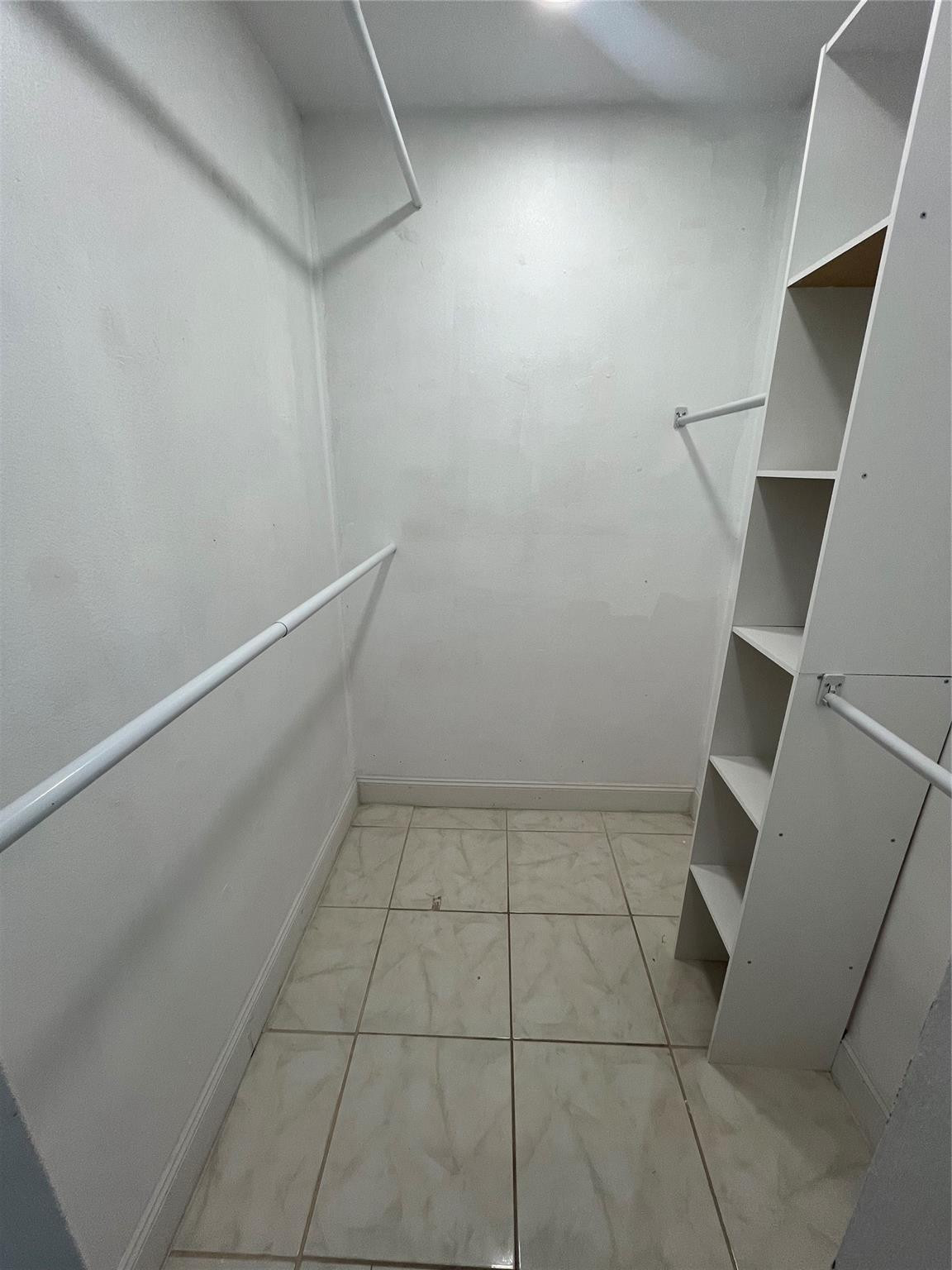 Walk-in closet with tiled flooring, hanging rods, and built-in shelving.