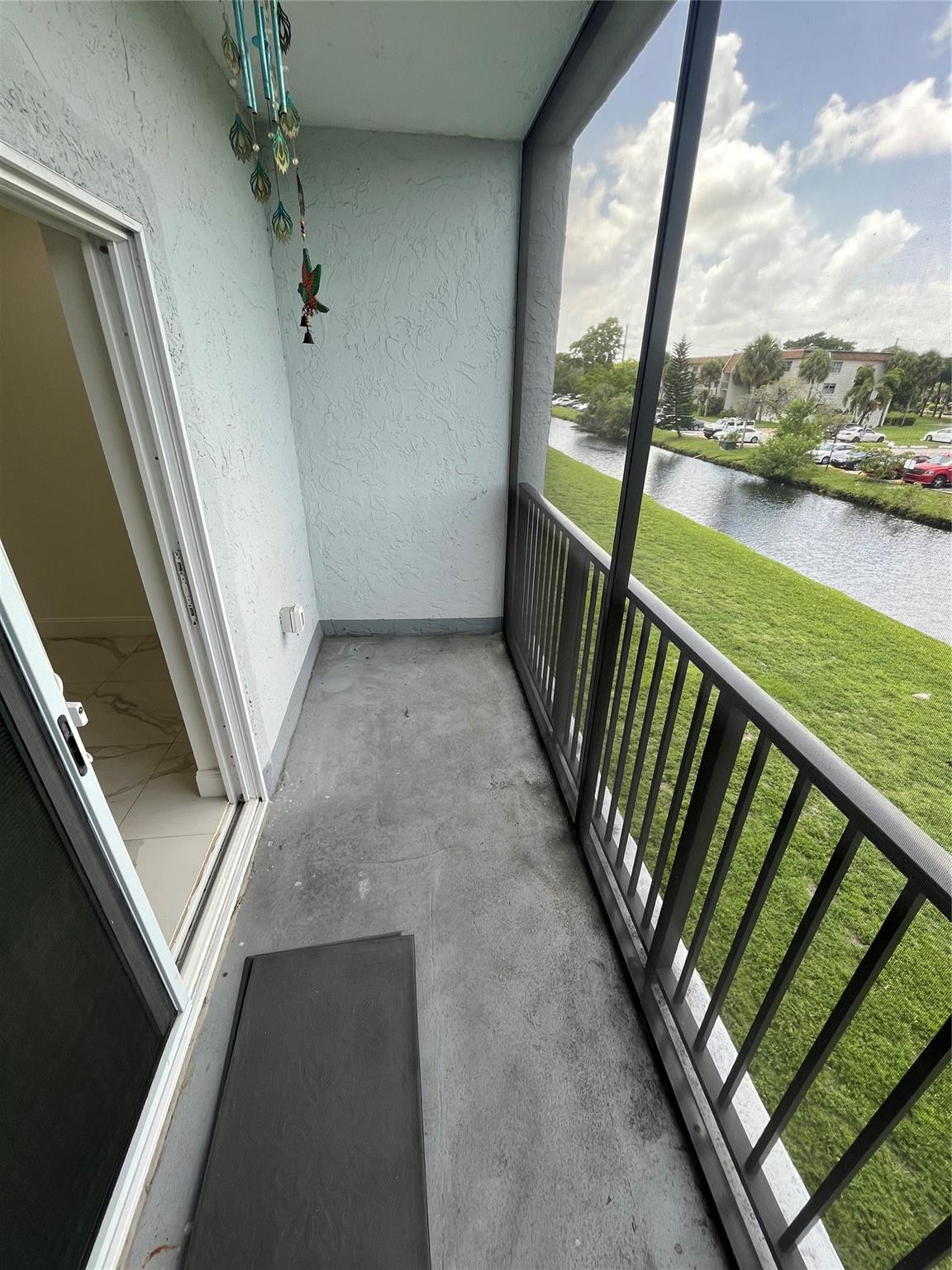 Concrete balcony overlooking a canal, with a black railing and hanging wind chime.