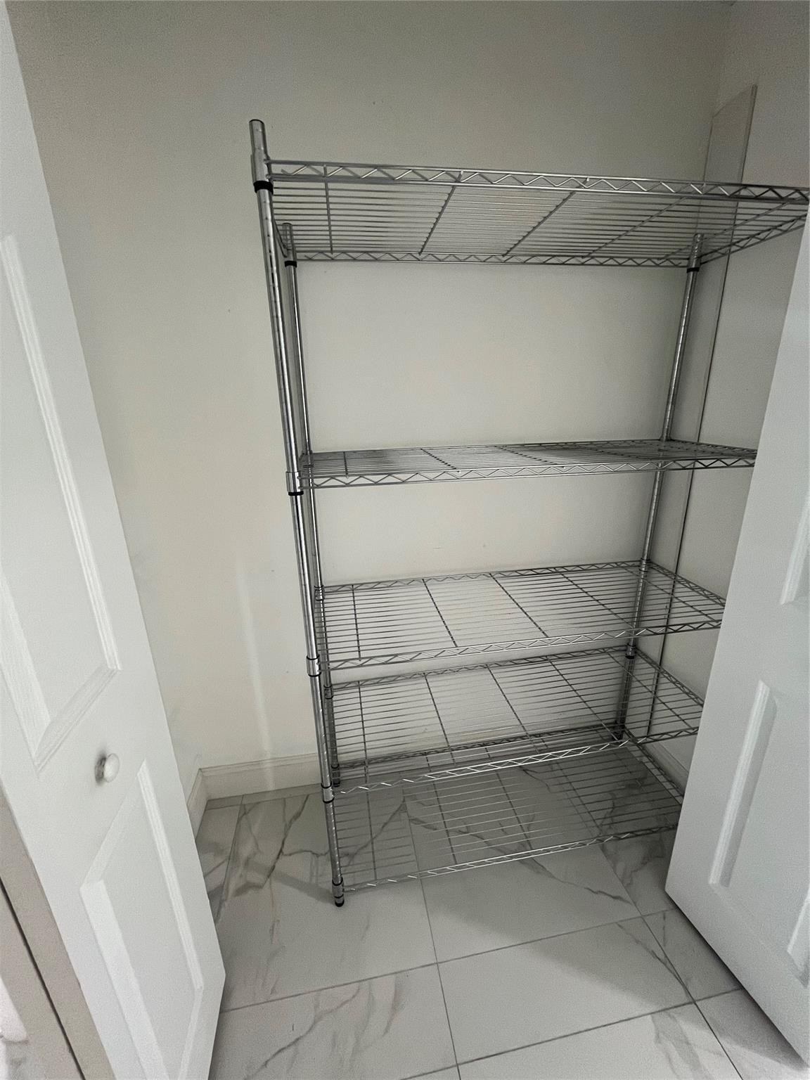 Walk-in closet with chrome wire shelving and large veined tile flooring.