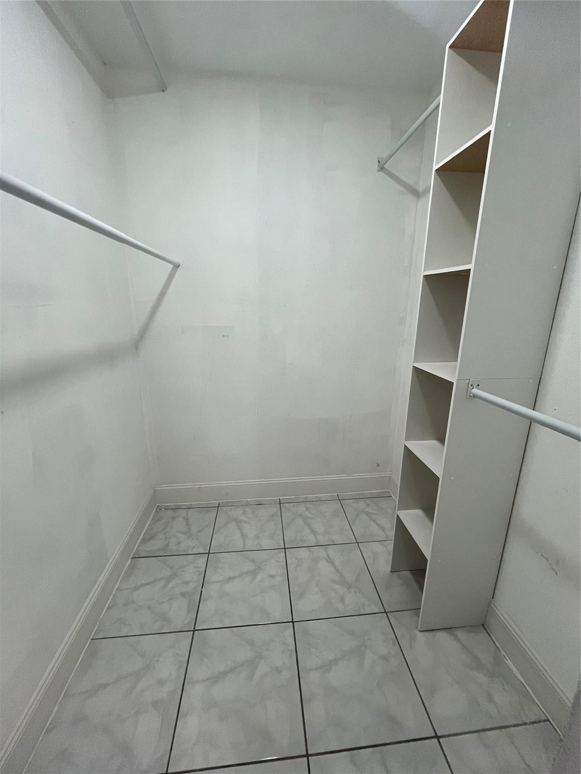Empty walk-in closet with built-in shelving, hanging rods, and patterned tile flooring.