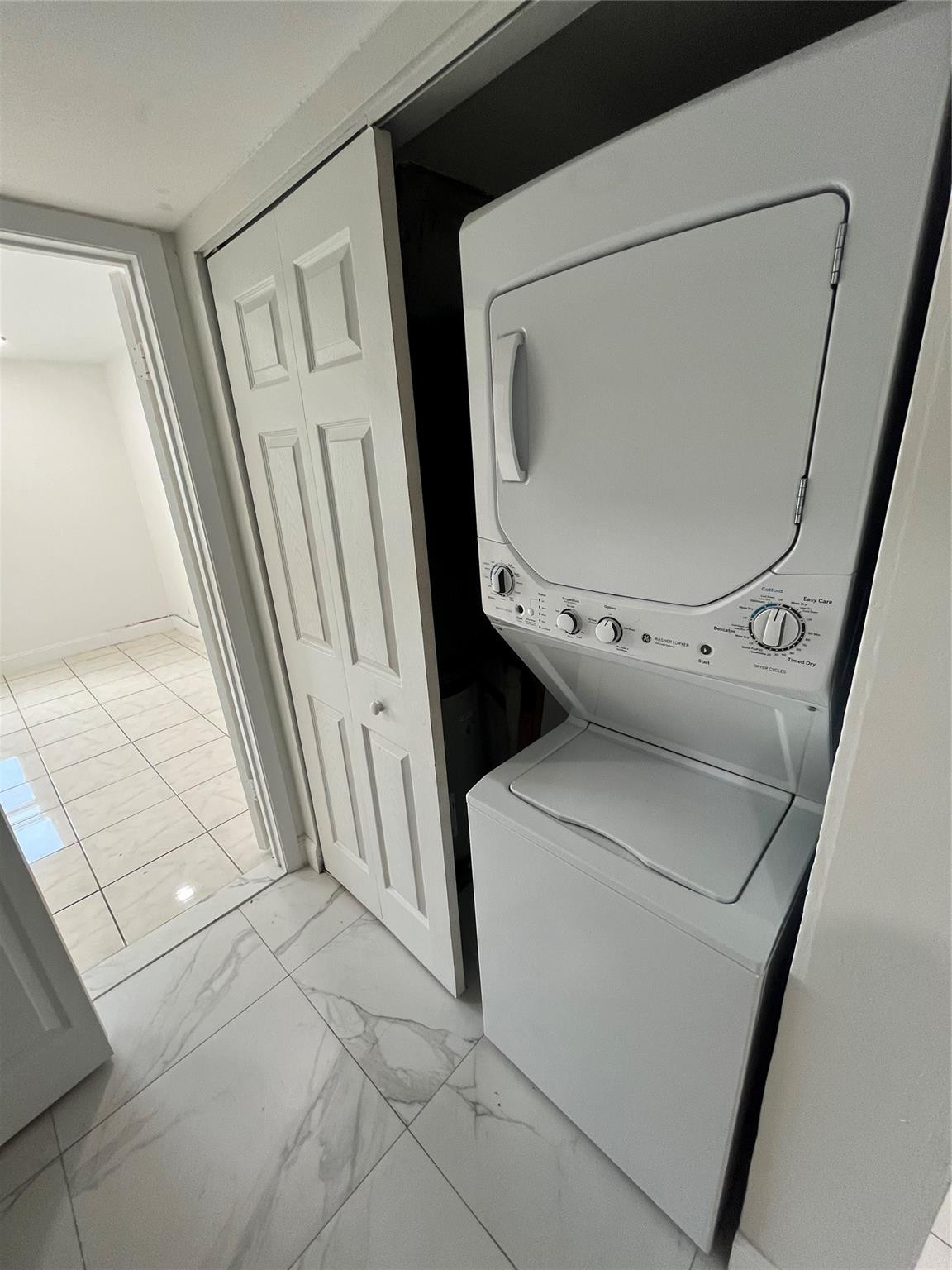 Stacked washer and dryer in a closet beside marble-look tile flooring.