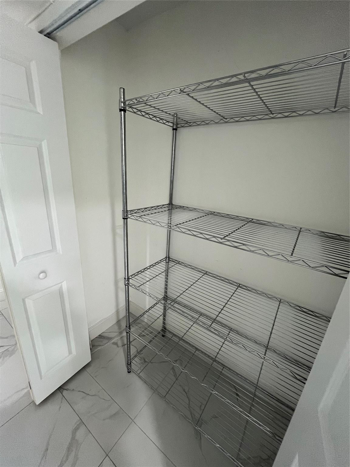 Closet with tall chrome wire shelves and gray veined tile flooring.