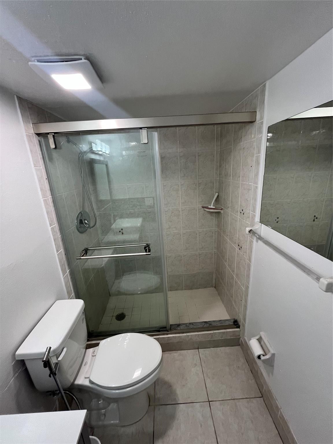 Bathroom with a glass-enclosed tiled shower, handheld showerhead, and toilet.