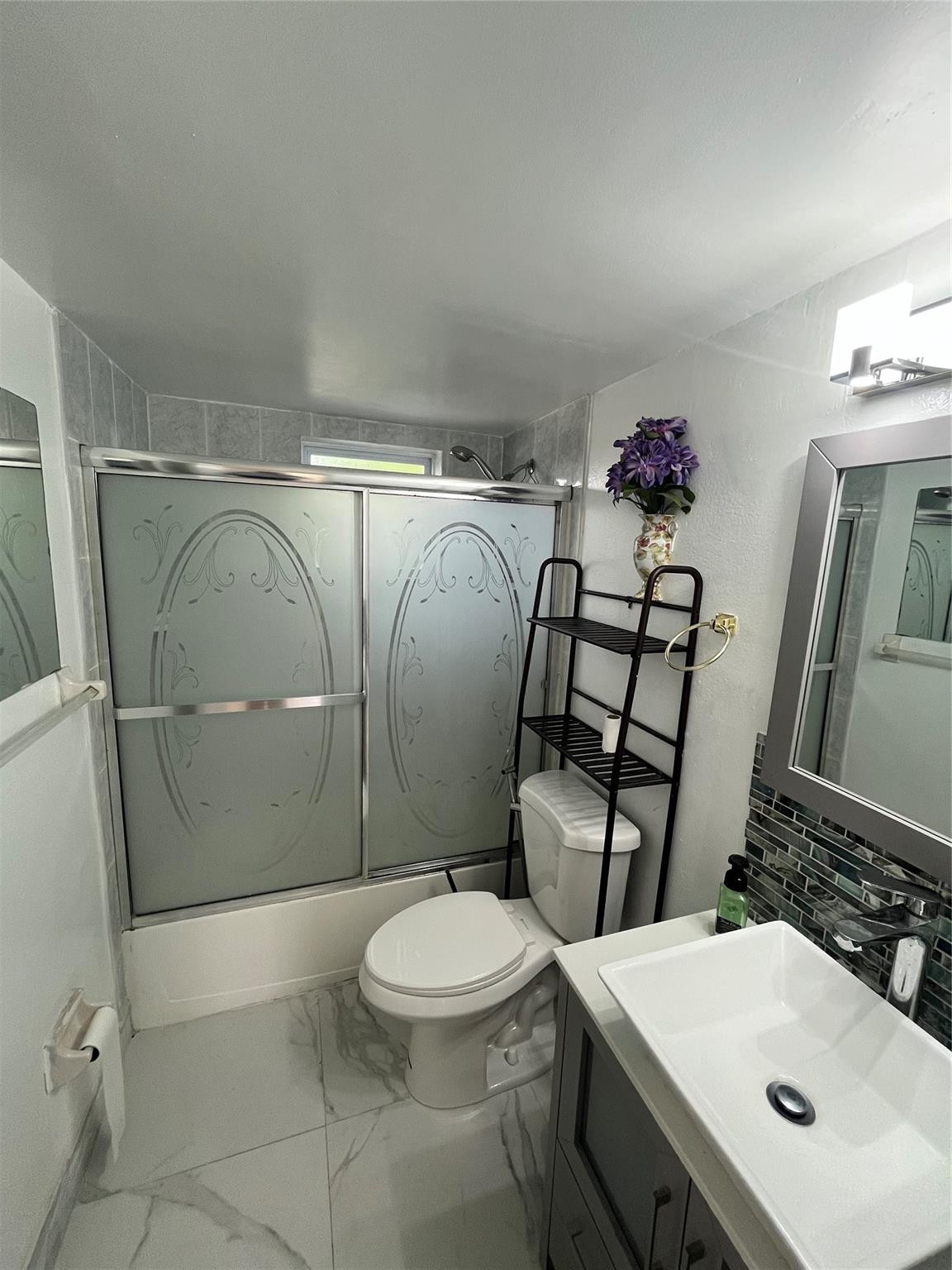 Bathroom with frosted sliding shower doors, a toilet, and a white vanity with dark mosaic backsplash.