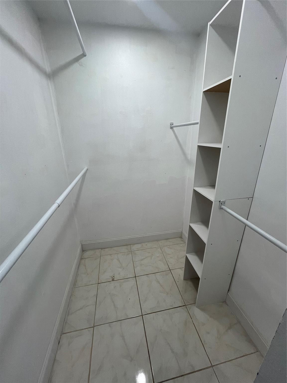 Walk-in closet with tiled floors, hanging rods, and built-in open shelving.