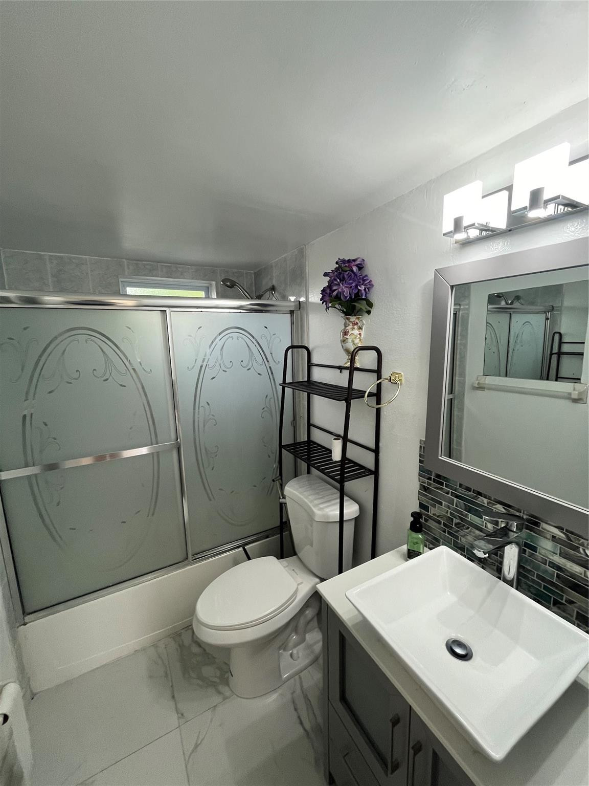 Bathroom with frosted sliding shower doors, a vessel sink, and dark mosaic backsplash.