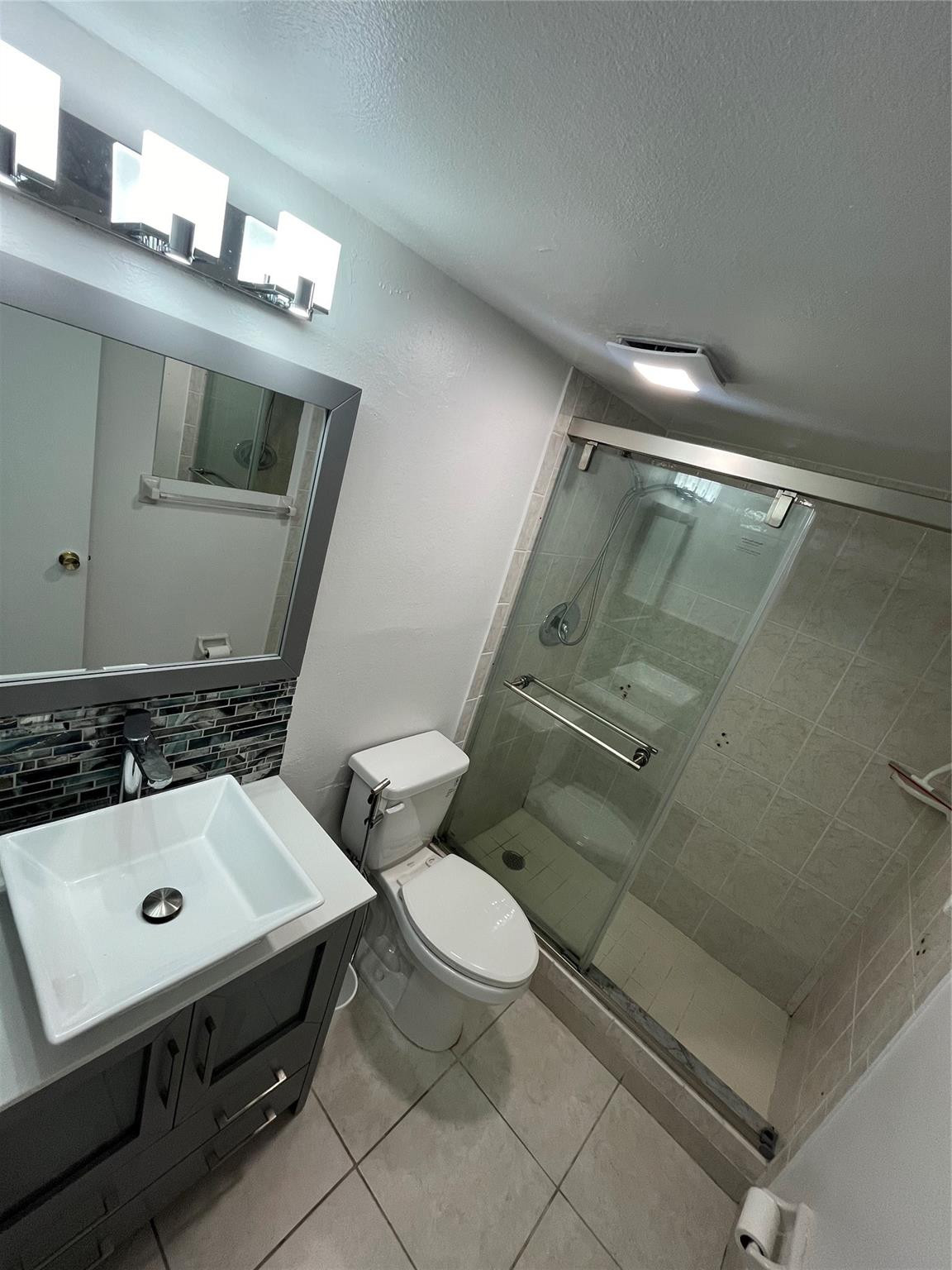 Bathroom with a dark vanity, white vessel sink, toilet, and glass-enclosed tiled shower.