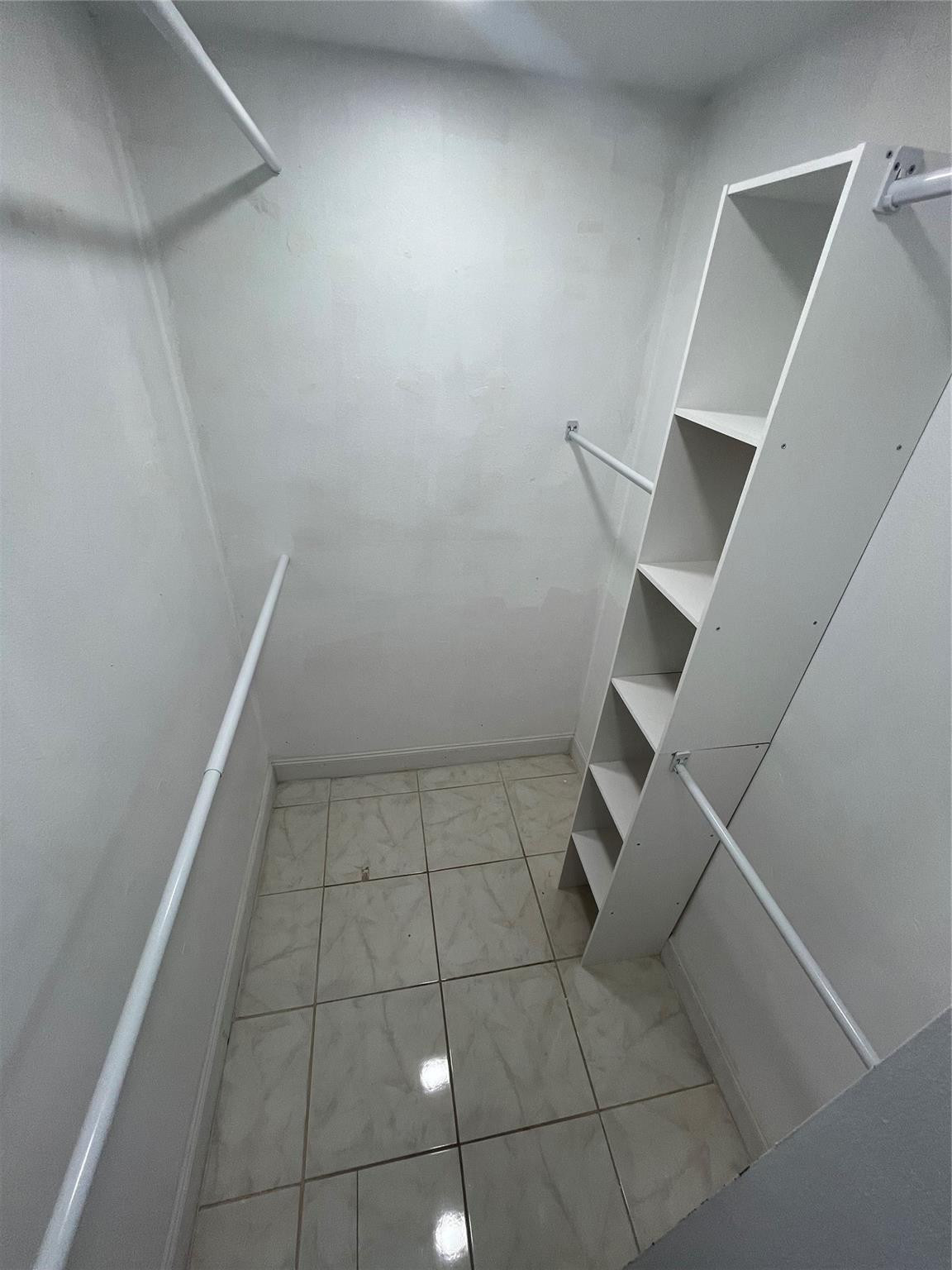 Empty walk-in closet with built-in shelving, hanging rods, and a tiled floor.