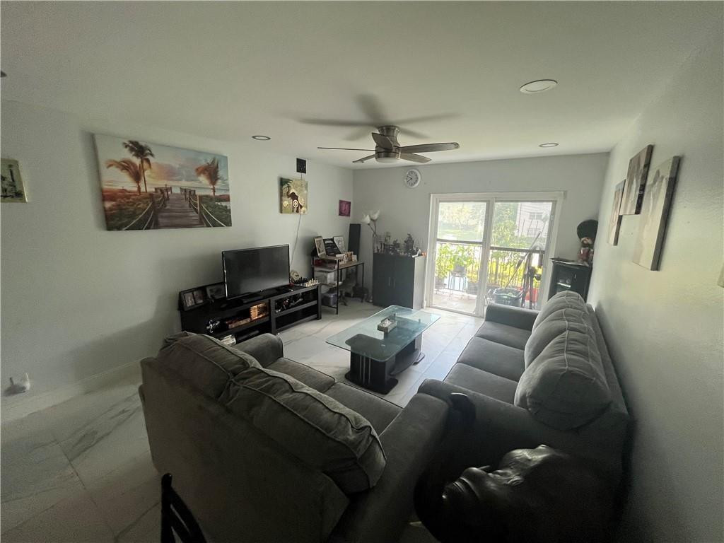 Furnished living room with gray sectional sofas, a ceiling fan, and sliding glass doors to a balcony.