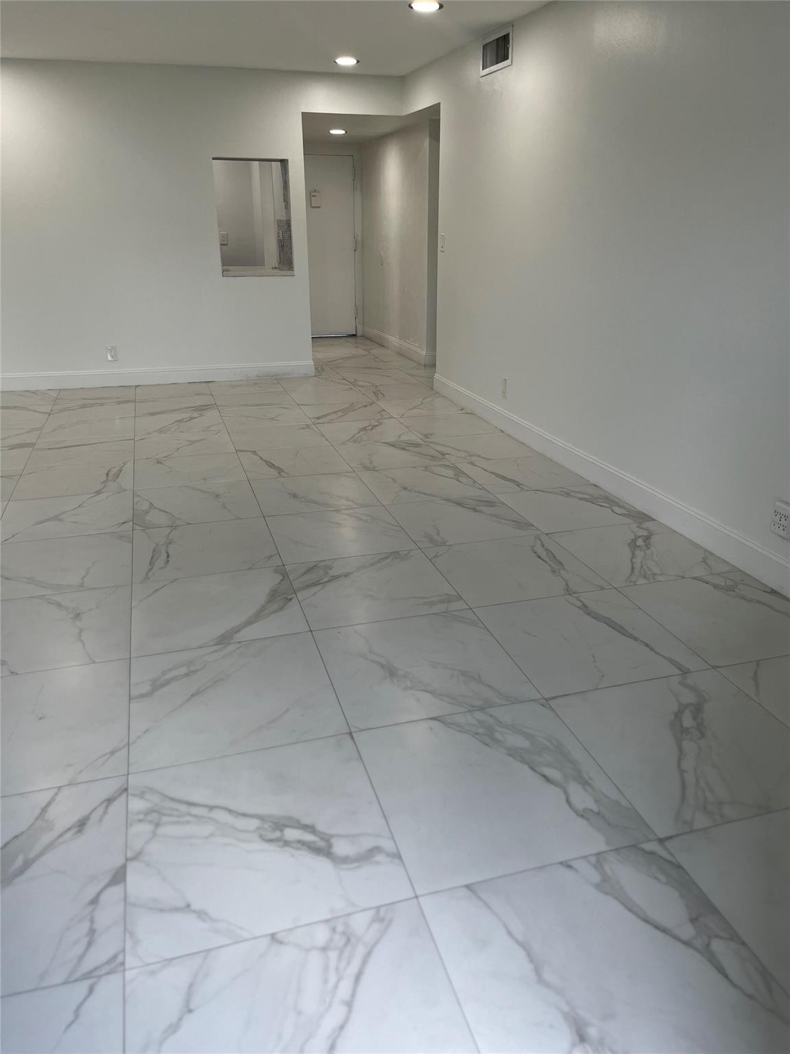 Empty room with large veined tile flooring and a pass-through opening.