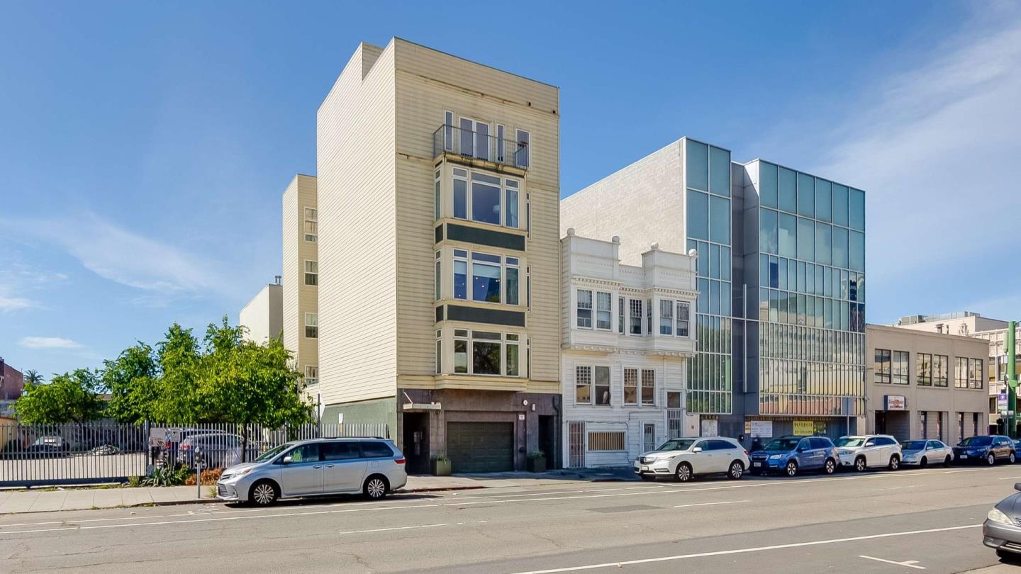 Beige multi-story building with projecting windows and a small balcony on a street lined with parked cars.