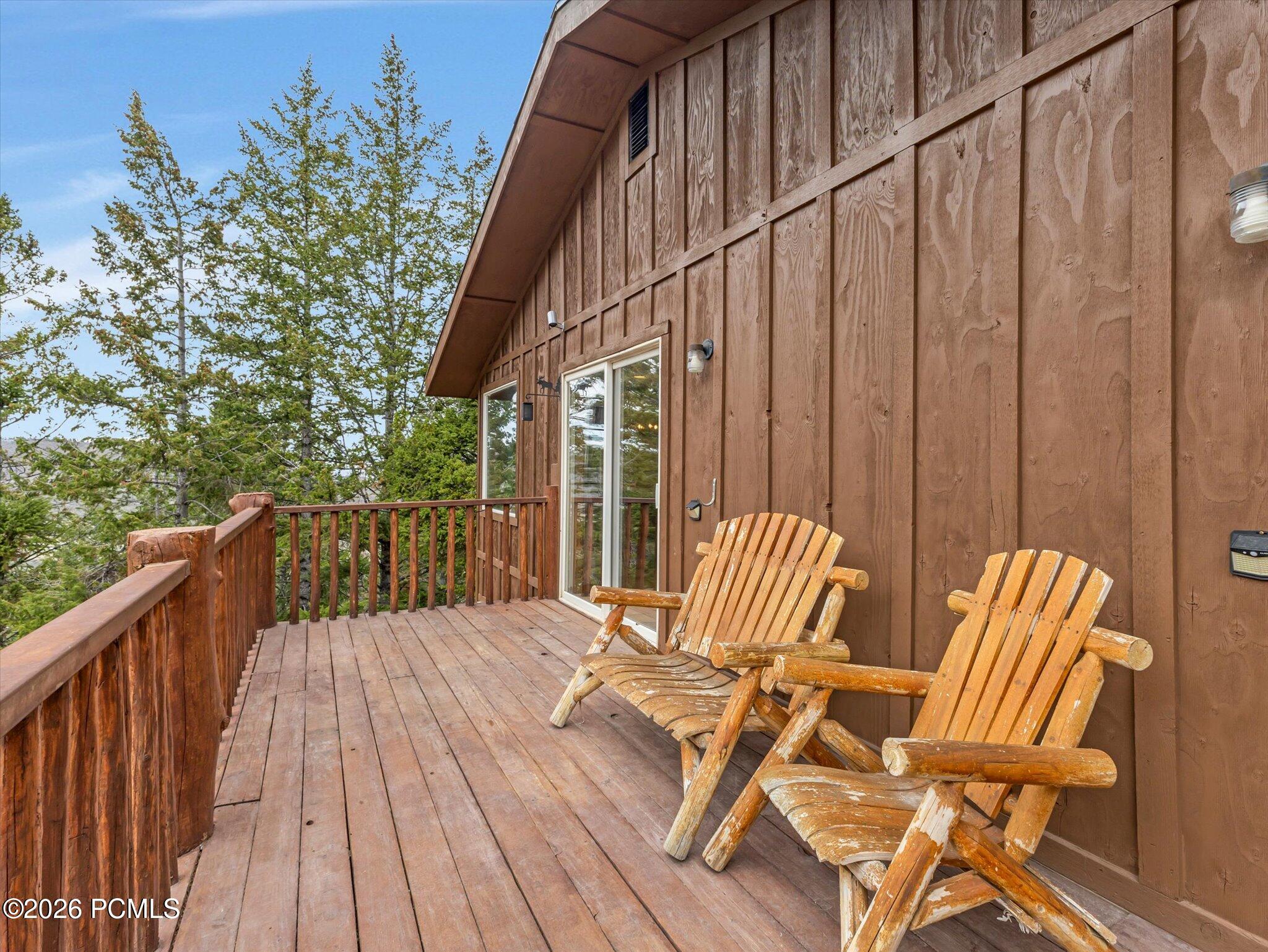 Wooden deck with two Adirondack chairs overlooking trees beside a brown-sided home.