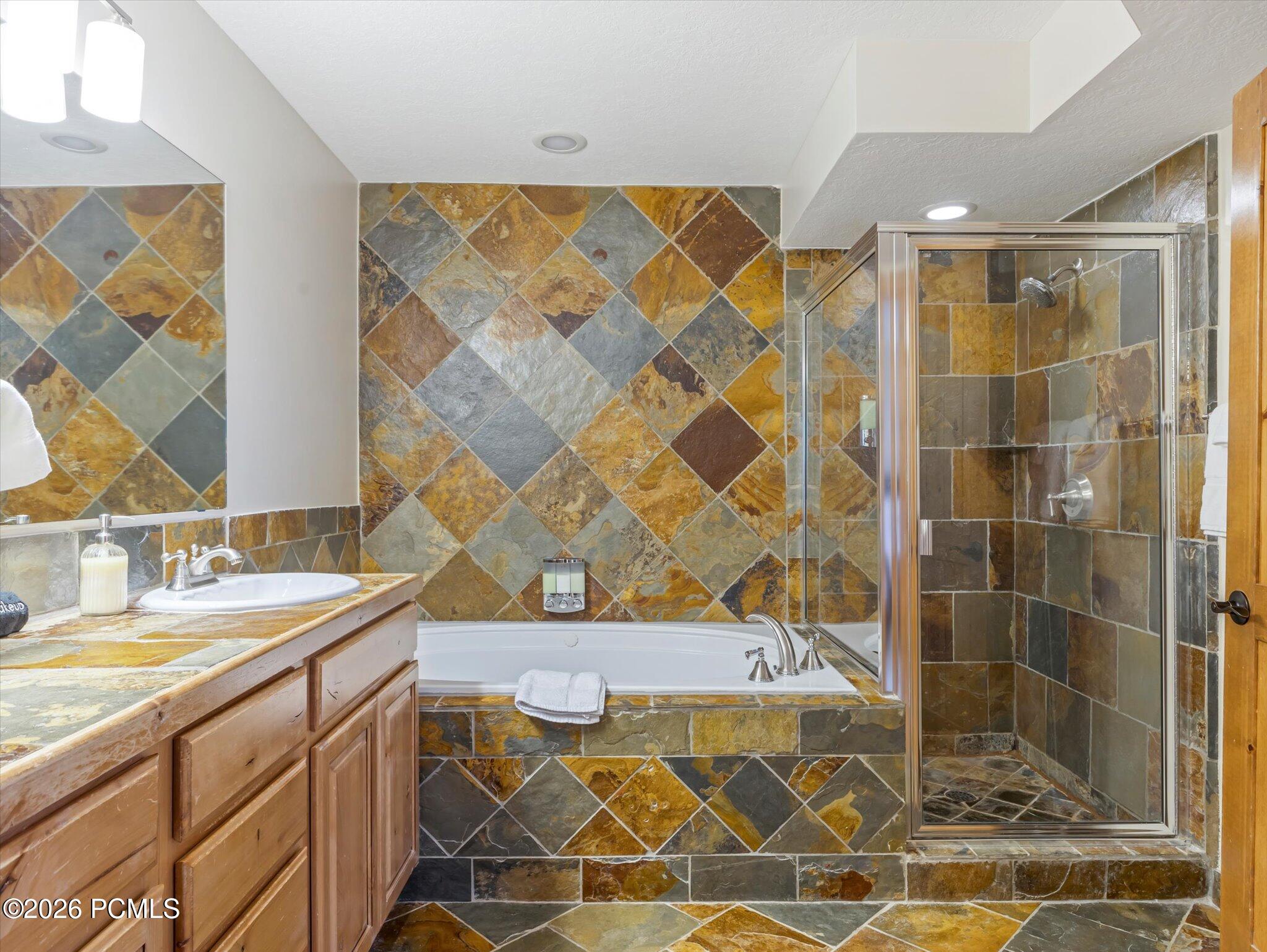 Bathroom with a slate-tiled tub and glass shower beside a wood vanity.