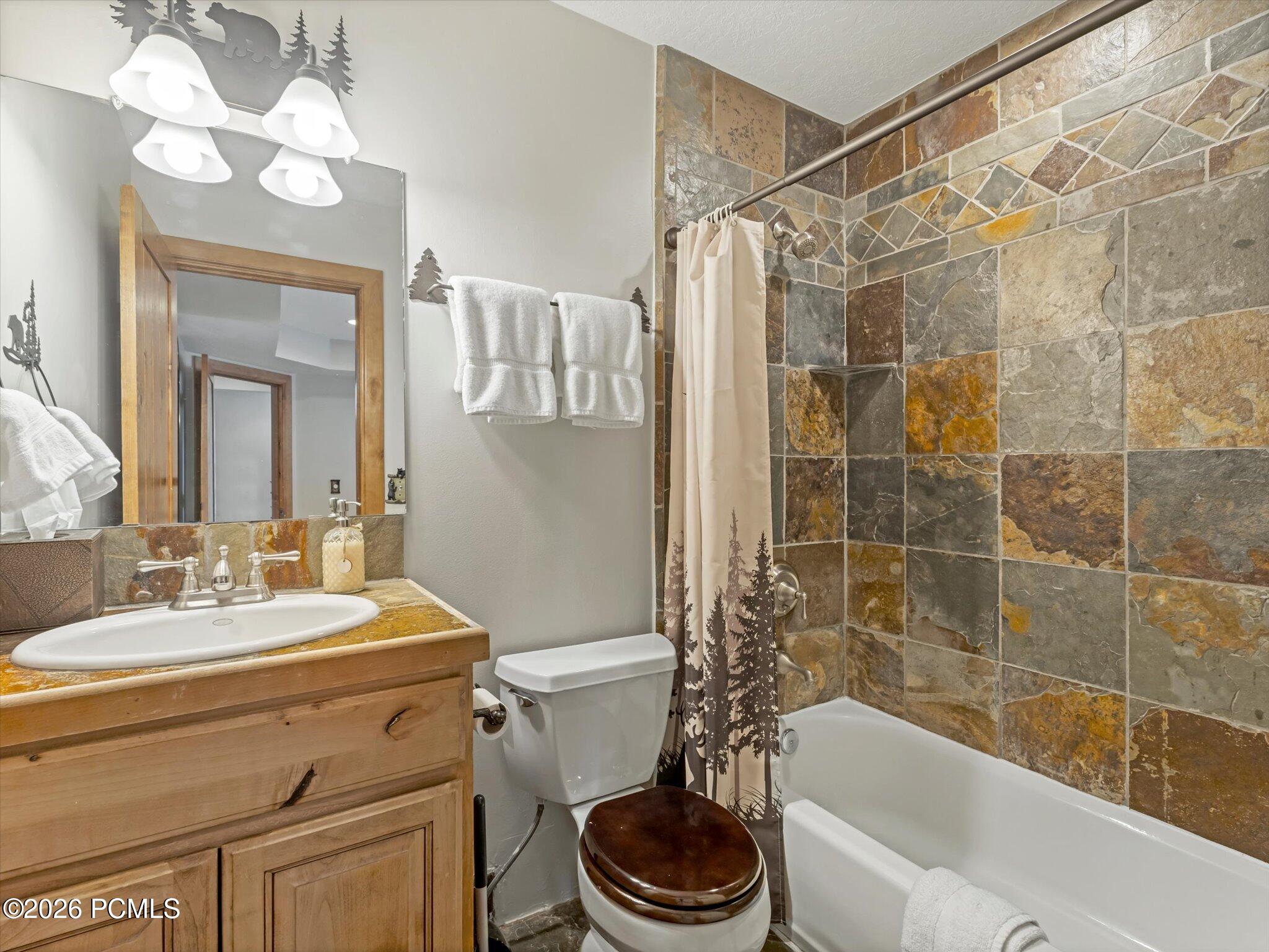 Bathroom with a wood vanity and sink beside a stone-tiled bathtub and shower.