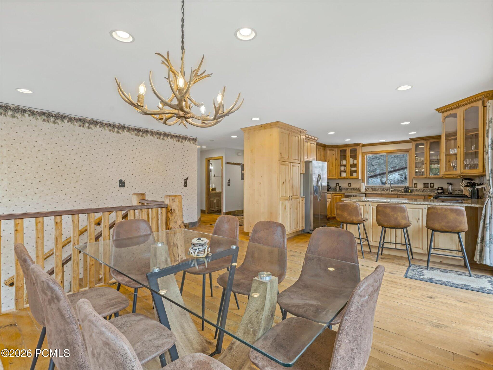 Dining area with a glass table and antler chandelier beside a wood-cabinet kitchen.