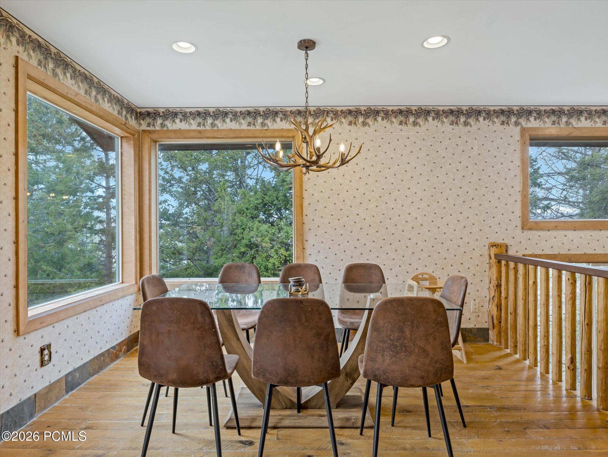 Dining room with a glass table, antler chandelier, large windows, and rustic wood railing.