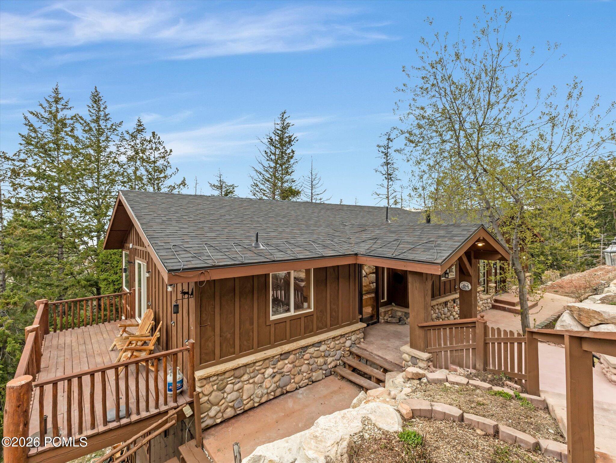 Rustic timber home with a stone foundation, raised deck, and covered entry among trees and rocks.