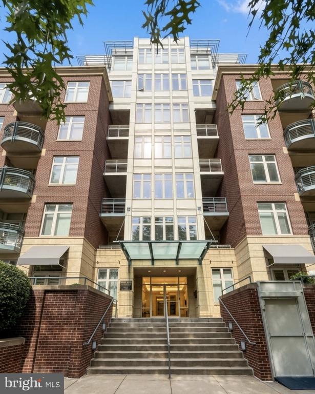 Condominium entrance with broad steps, a glass canopy, and brick-and-stone facade.