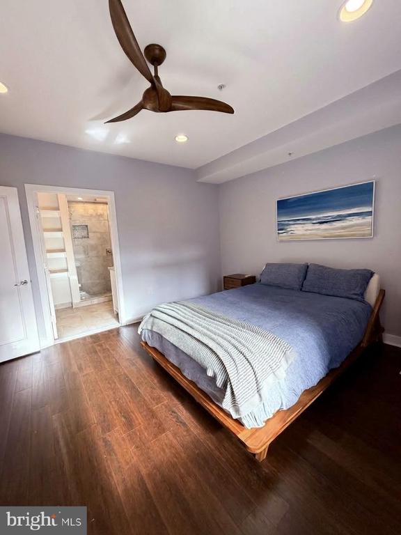 Bedroom with a wood platform bed, gray bedding, ceiling fan, and doorway to an ensuite bathroom.