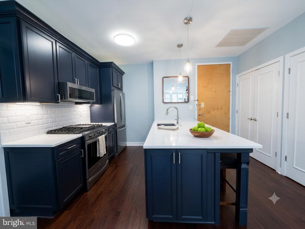 Kitchen with navy cabinets, stainless-steel appliances, and a large white island topped with green apples.