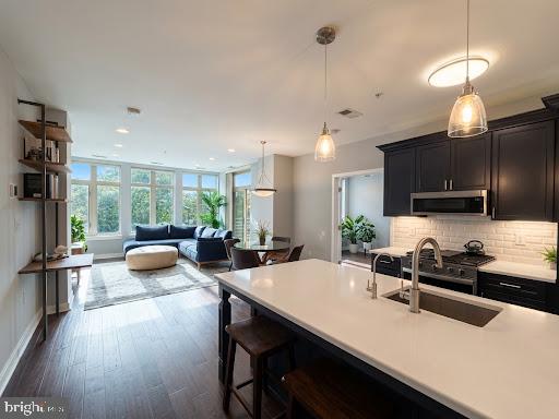 Open-plan kitchen with a large white island, dark cabinets, and a bright living area by tall windows.